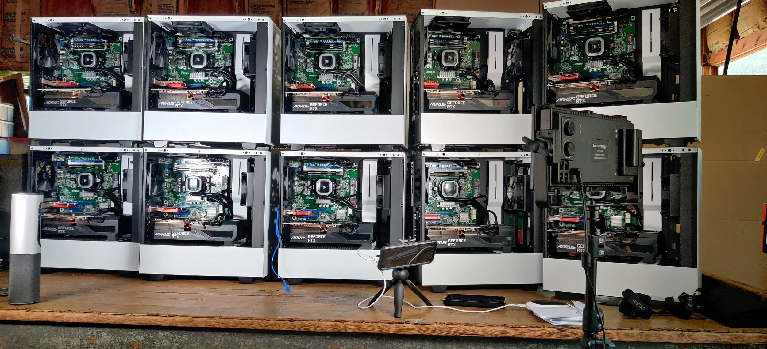 A collection of eight computer graphics cards and motherboards being assembled or prepared, arranged in two rows on a workbench, with some computer accessories and tools nearby.