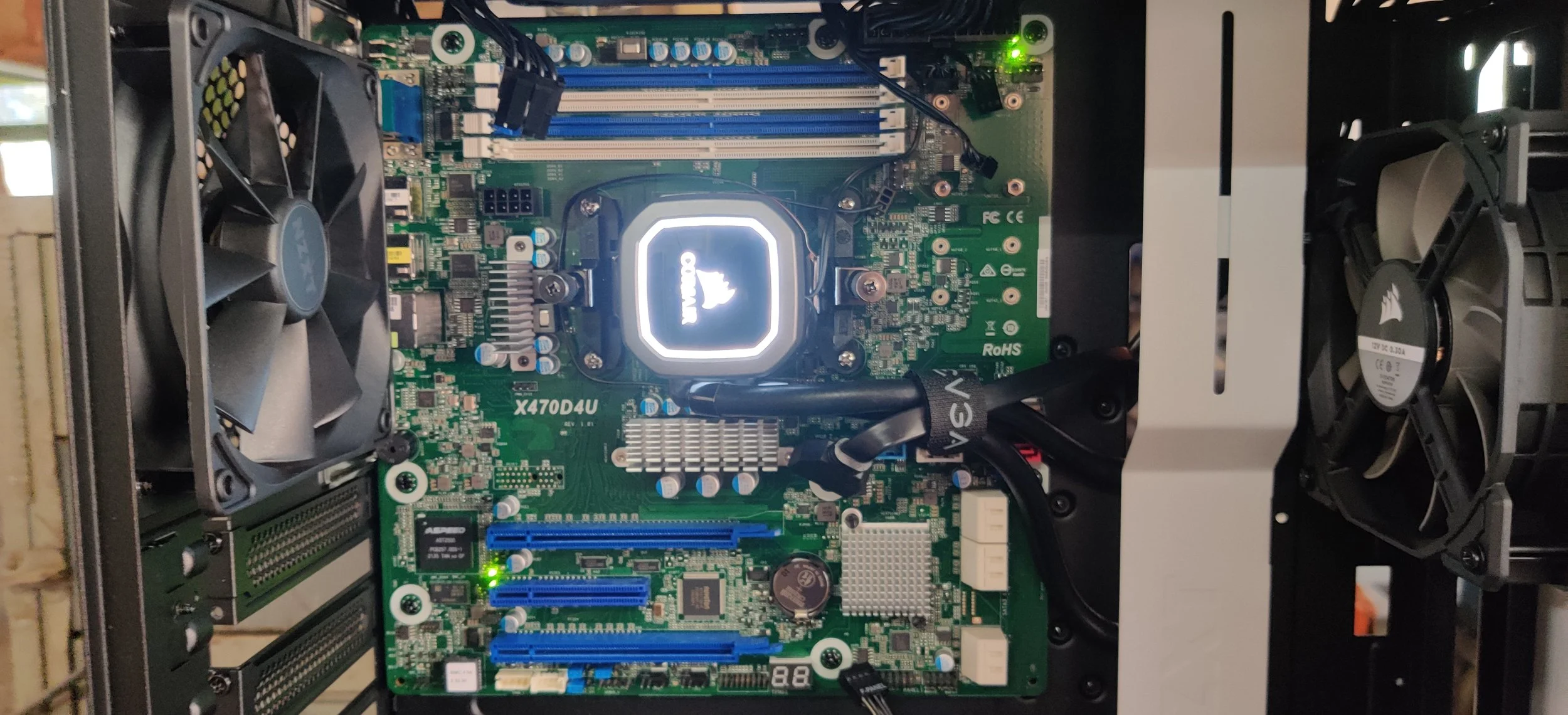 Inside a computer case showing a green motherboard with various components, two cooling fans on each side, with a central illuminated CPU cooler, and cables connected to the motherboard.