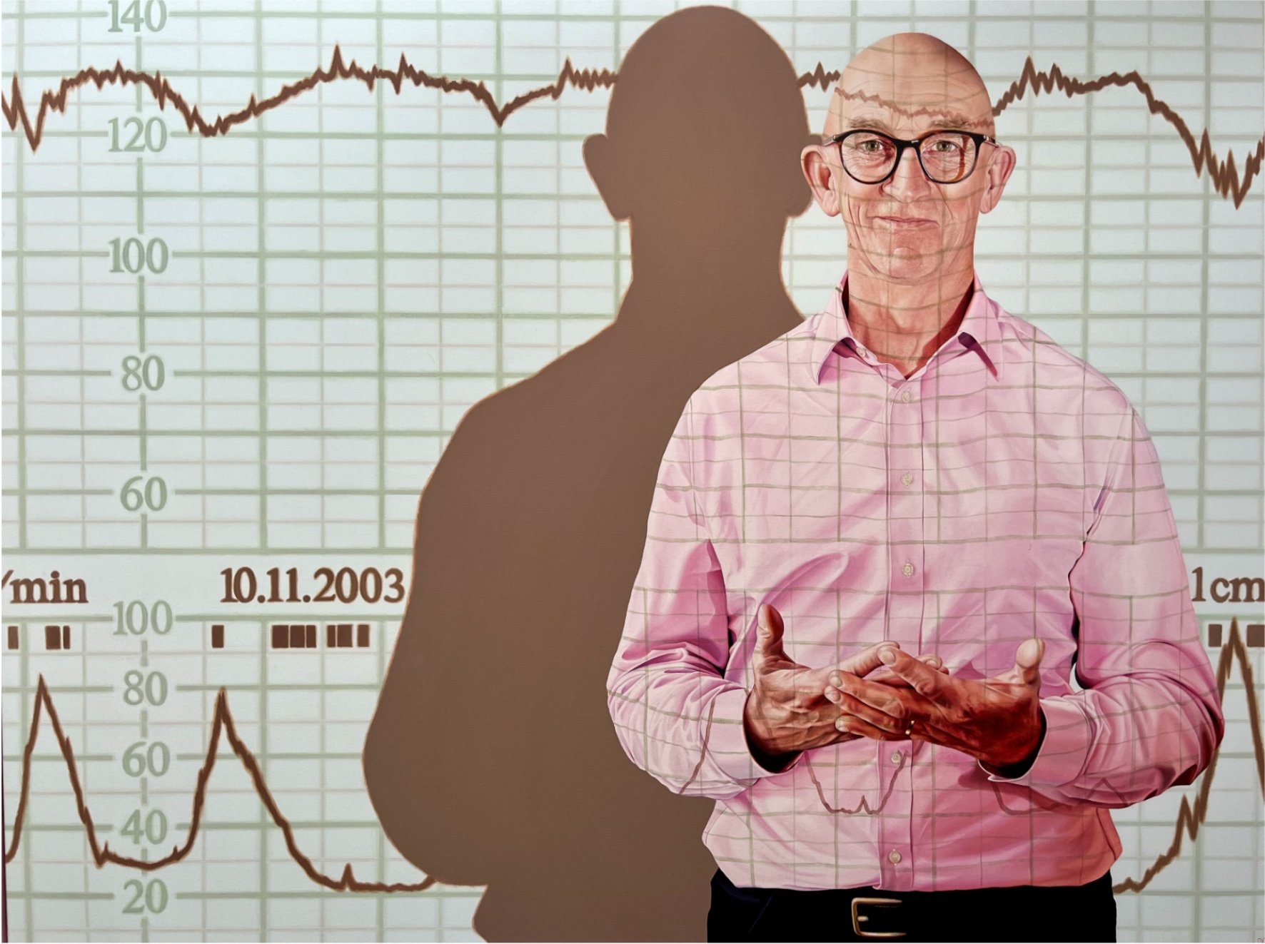 A male midwife in a pink checkered shirt stands in front of a medical chart showing a brain scan and EEG data, with his shadow cast on the chart. By Jen Darcy