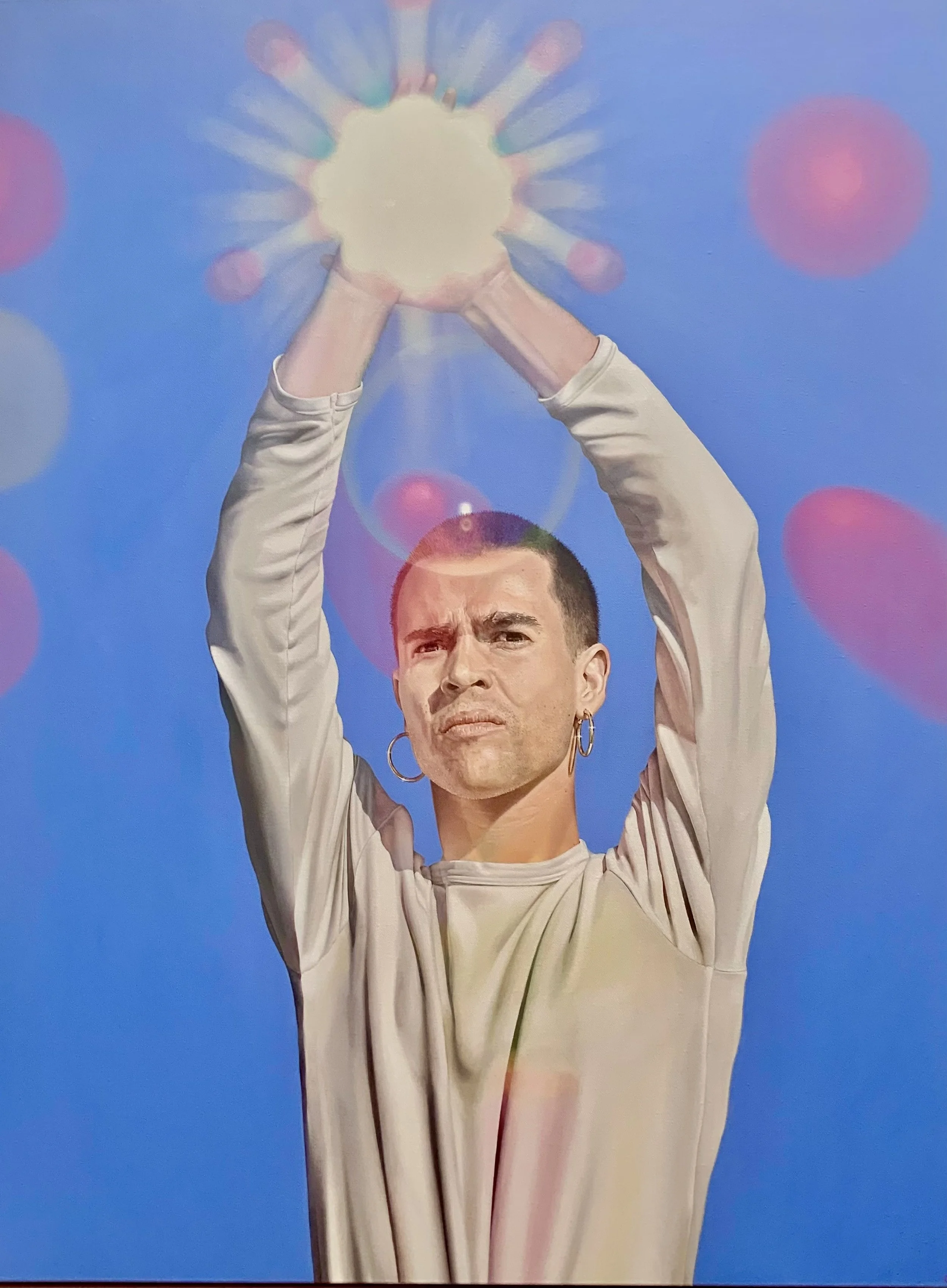 A man with short dark hair and hoop earrings raises his arms holding a bright, glowing orb of light against a blue background with pink and purple bokeh effects. By Jen Darcy
