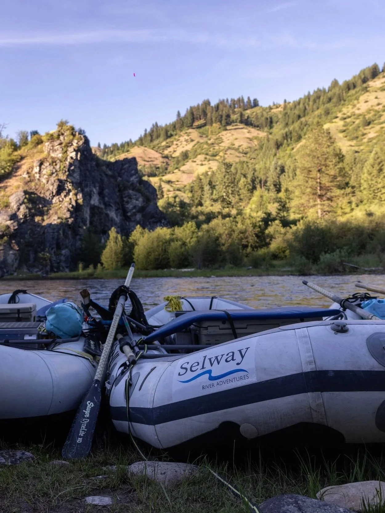 Two white rafts in the shade, on the river with the sunlight on the hills in the background.