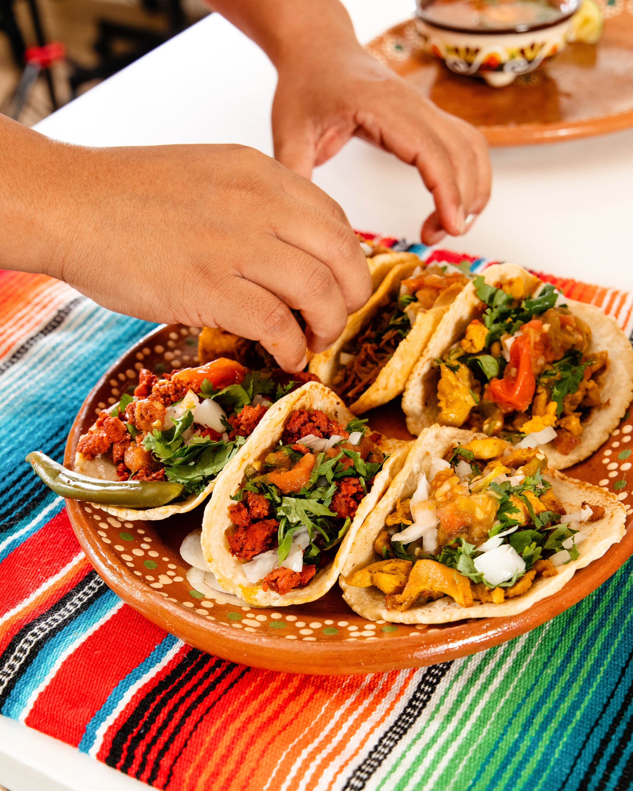 Person arranging Mexican tacos on a colorful, striped tablecloth.