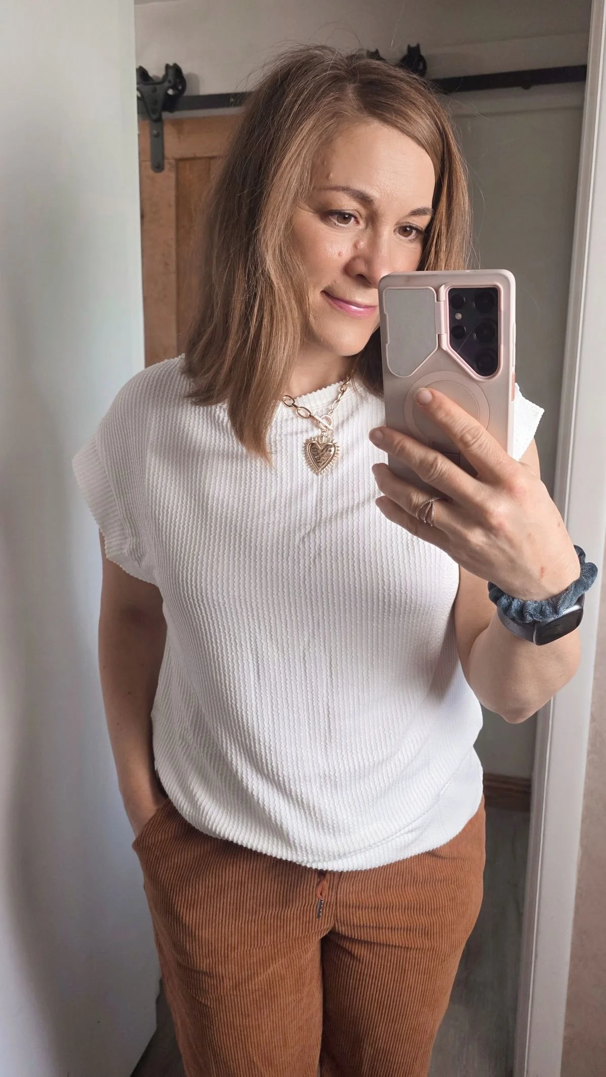 Mirror selfie of woman in white loose top with gold heart necklace.