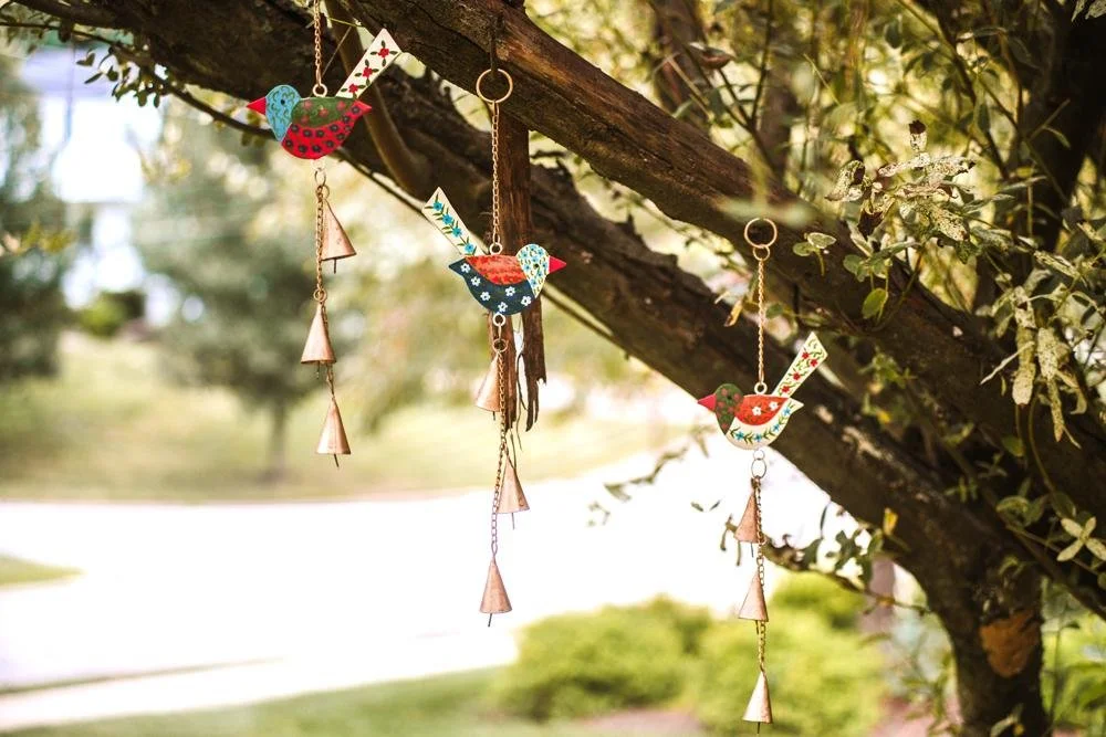 colorful bird wind chimes in shades of blue, orange and green, hanging from small tree limb.