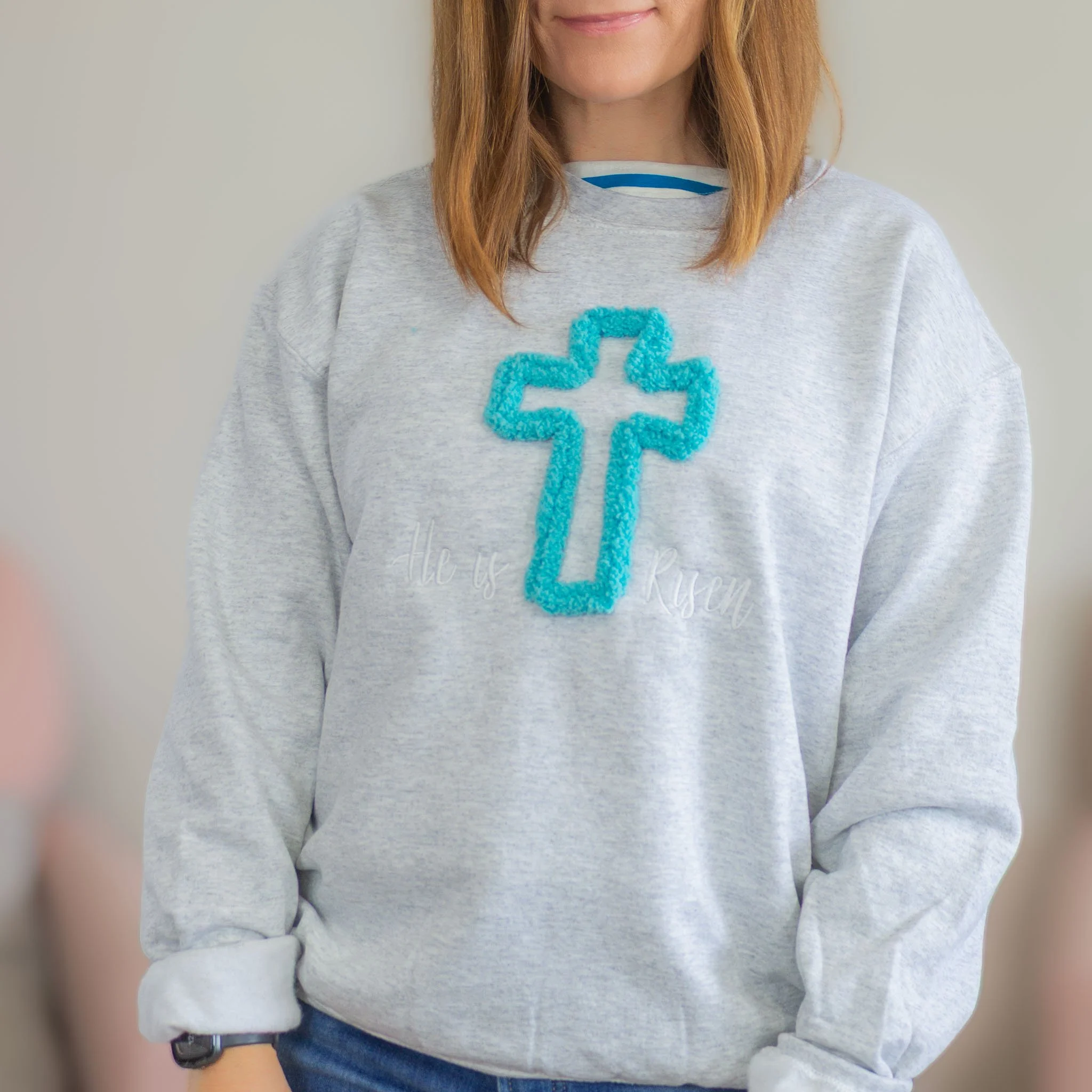 gray sweatshirt with teal chenille cross with words, "He is risen."