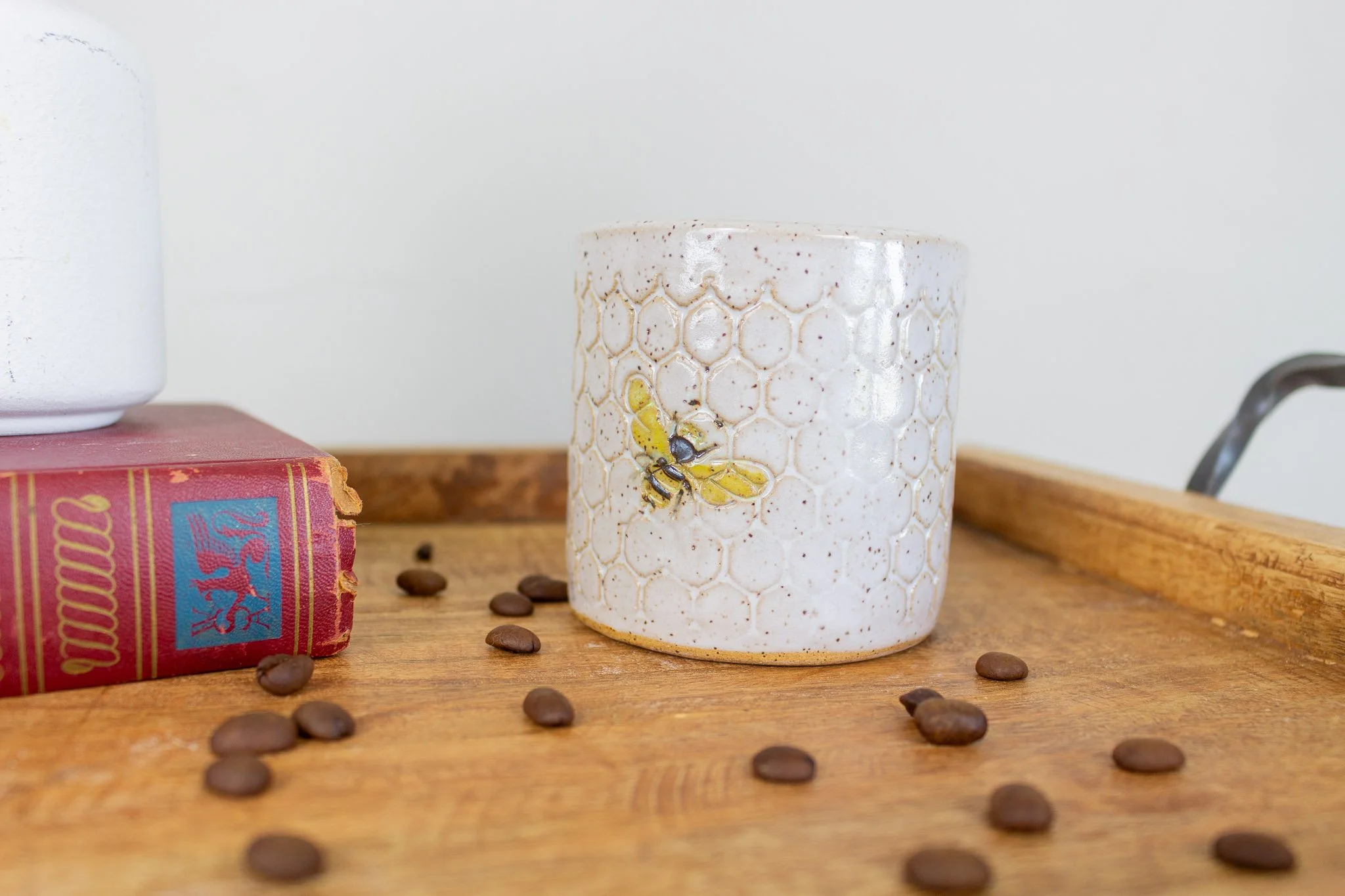 Side view of handmade ceramic mug with cream honeycomb design and small black and yellow bee flying upwards.