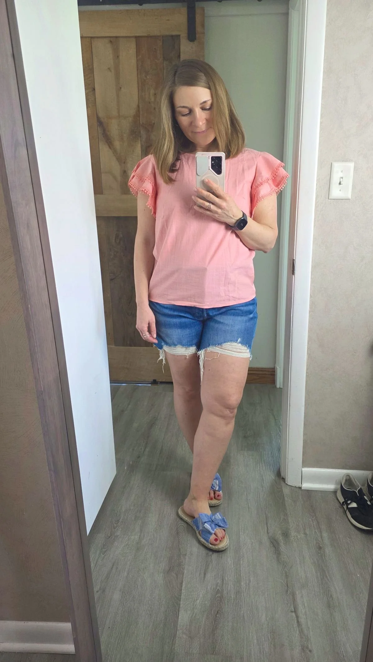 mirror selfie of woman in pink top with ruffled short sleeves.