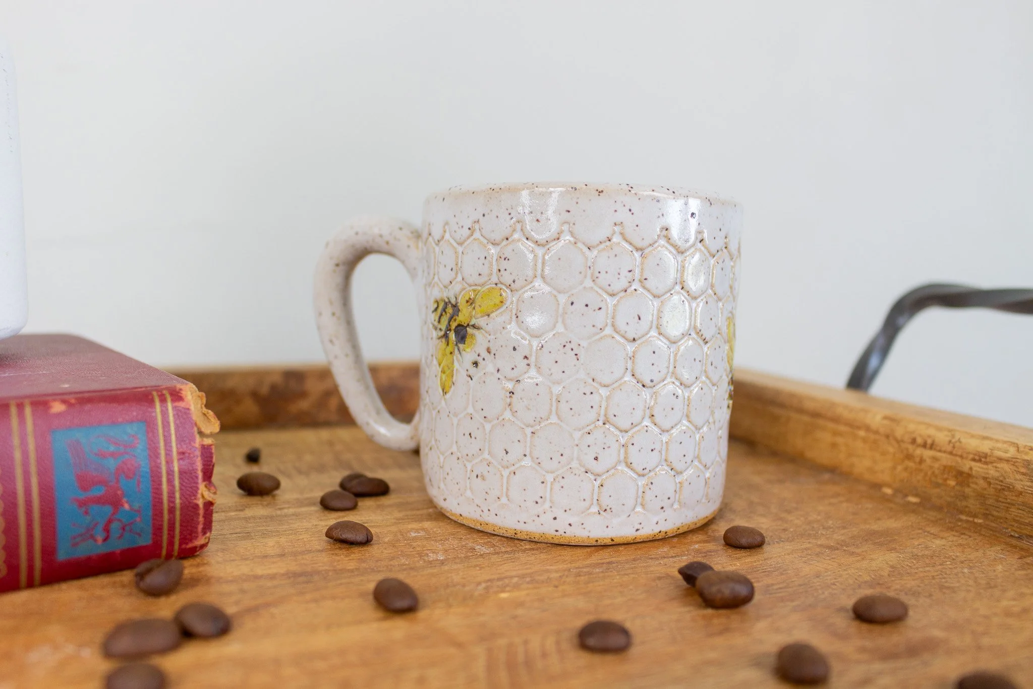 back of handmade ceramic mug with cream honeycomb design and small black and yellow bee flying upwards.