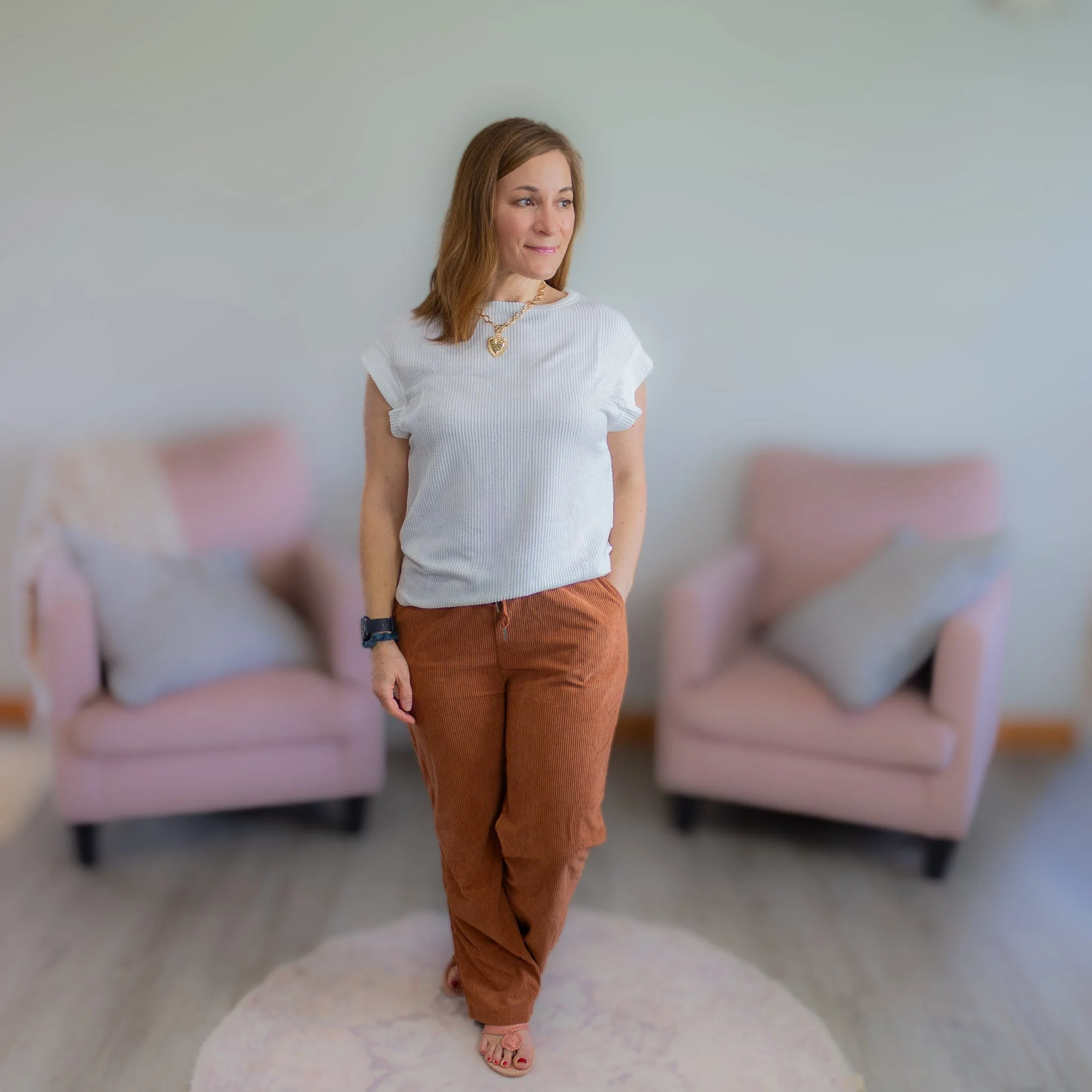 woman in outfit of white casual top, brown corduroy pants and gold necklace.
