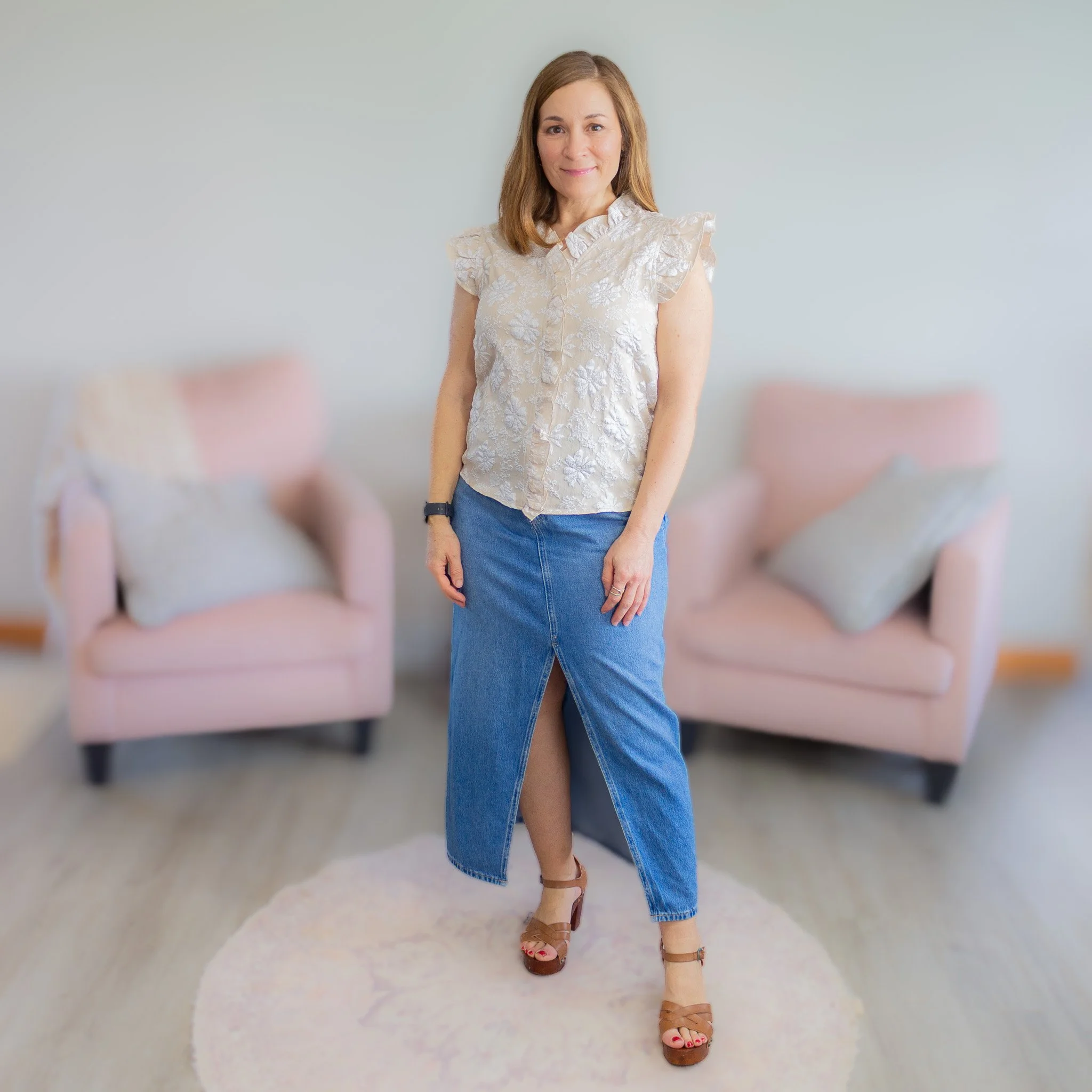 woman looking and smiling toward camera in sleeveless top and long denim skirt.