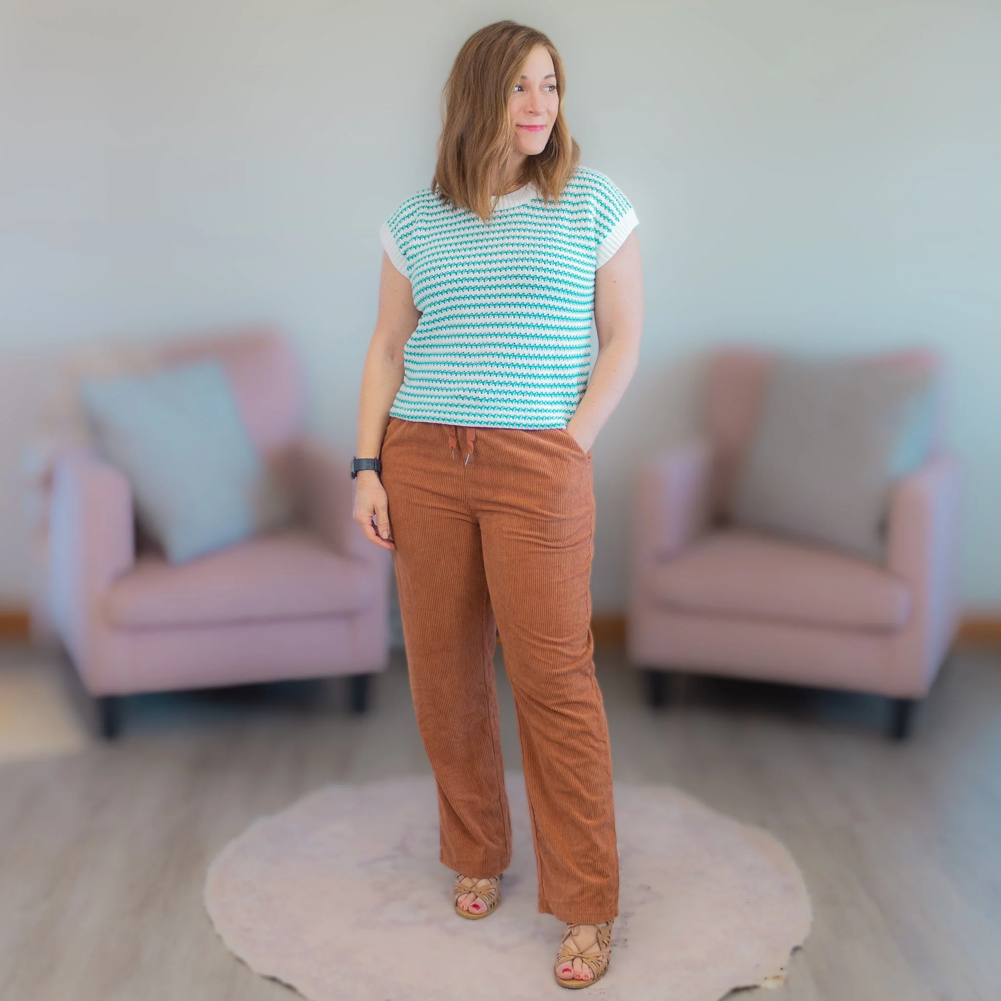 woman wearing green and white striped short sleeve sweater and brown pants looking to her left.