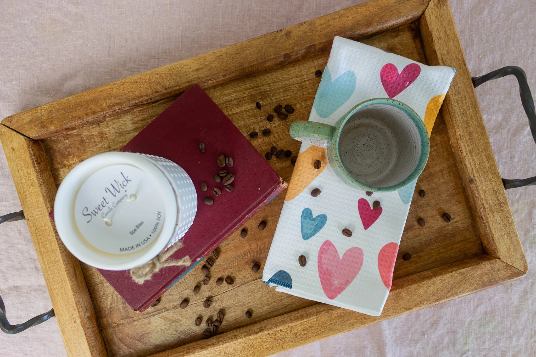 birds-eye view of tray holding mug, scattered coffee beans, candle and book.