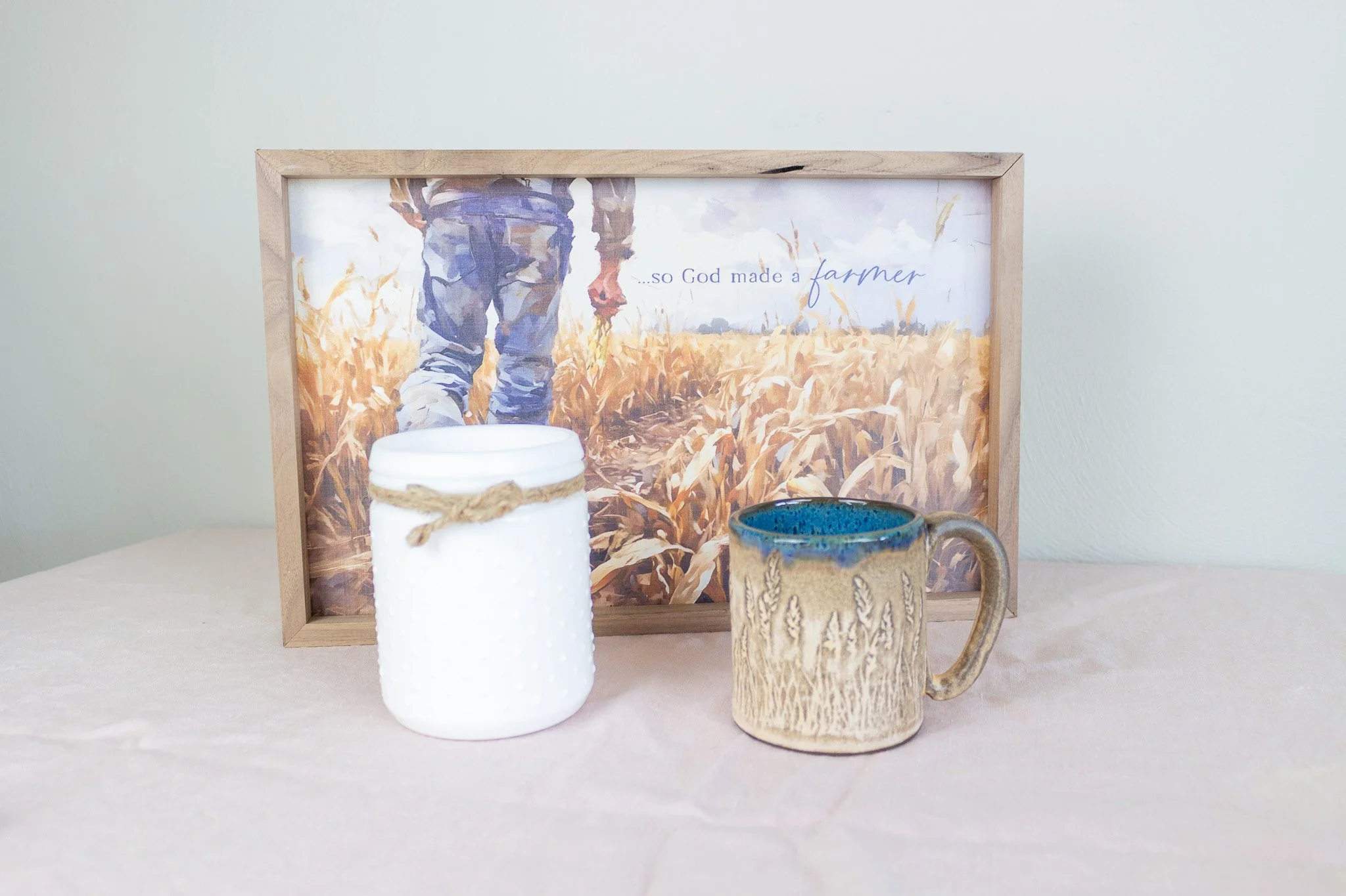 tan wheat mug with white candle and artwork that says "And God Made a Farmer."