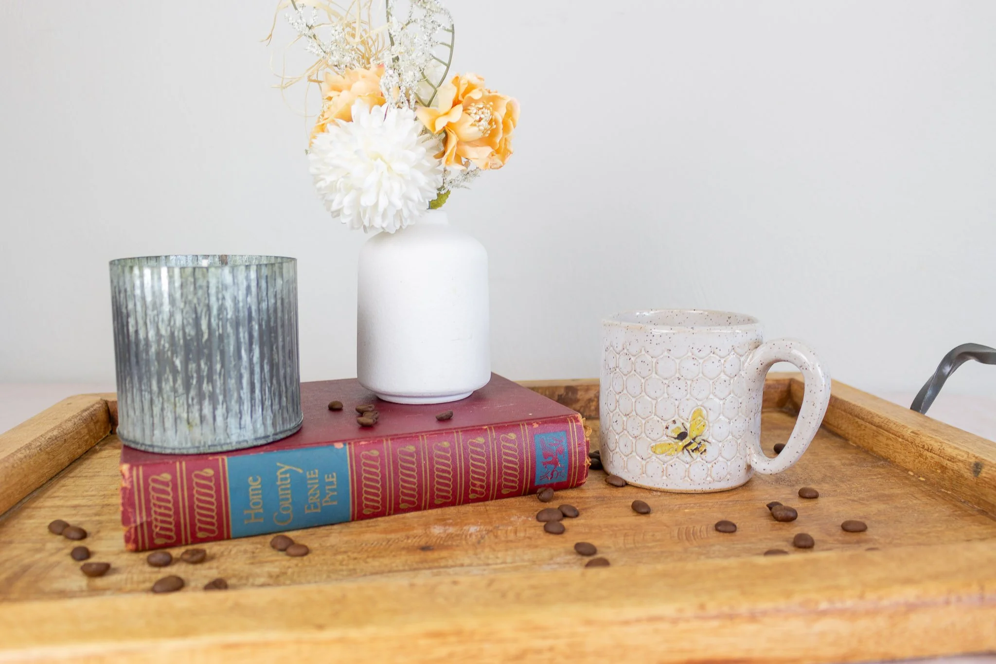 handmade bee mug on tray with candle, small vase of flowers and coffee beans.