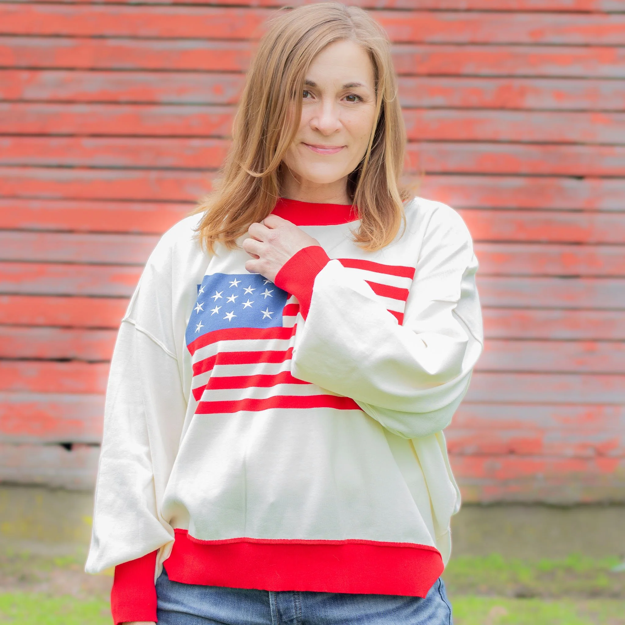 woman wearing white sweater with red trim and American flag across the chest.