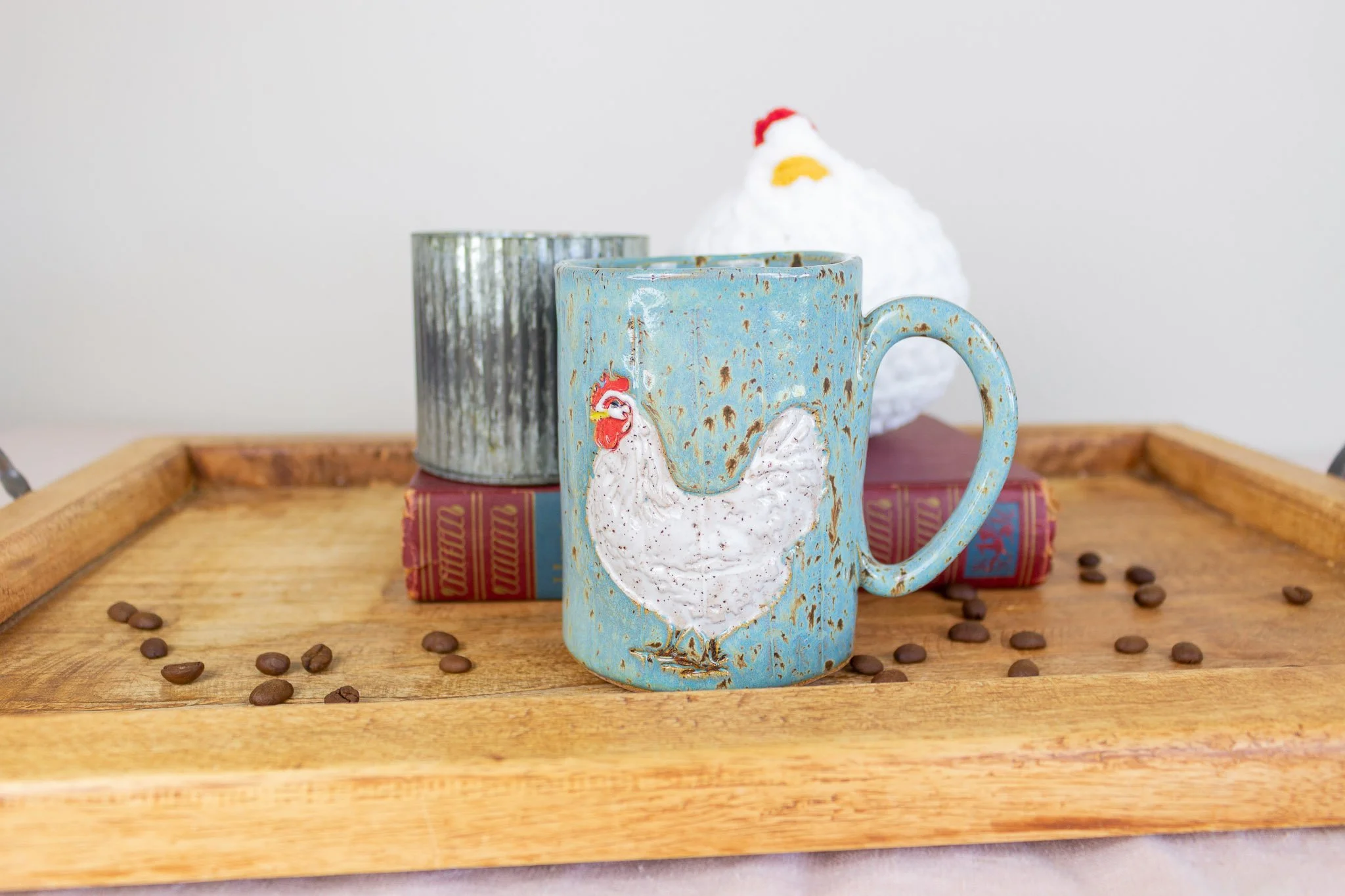 turquoise rooster mug on tray in front of candle and white plush rooster.