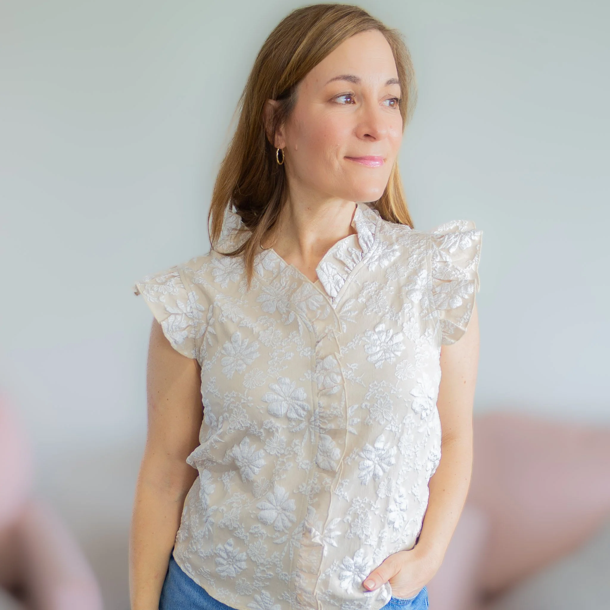 woman looking to the side from waist up in tan and white jacquard sleeveless top.