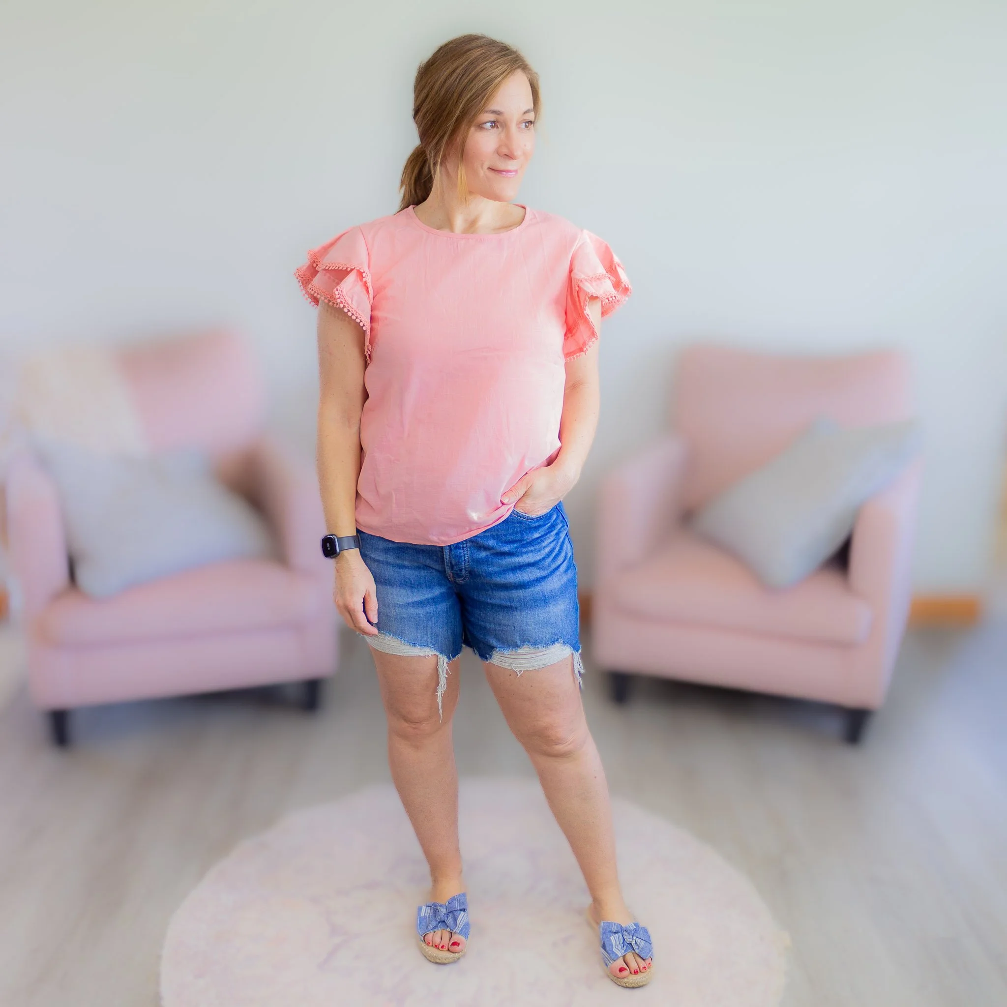 woman looking to side wearing cutoff jeans and pink top.