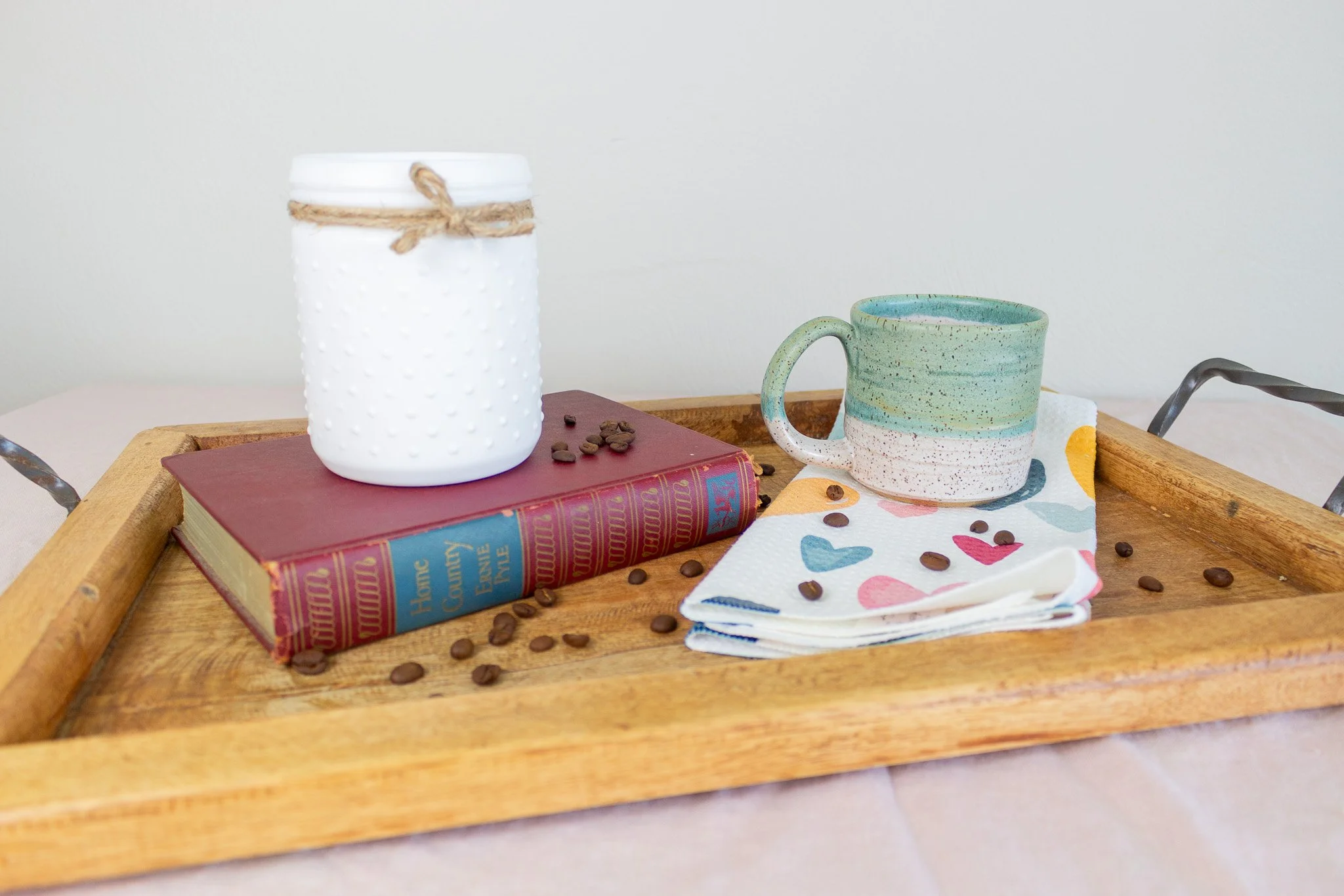 turquoise and cream mug sitting on colorful heart towel with coffee beans and candle.