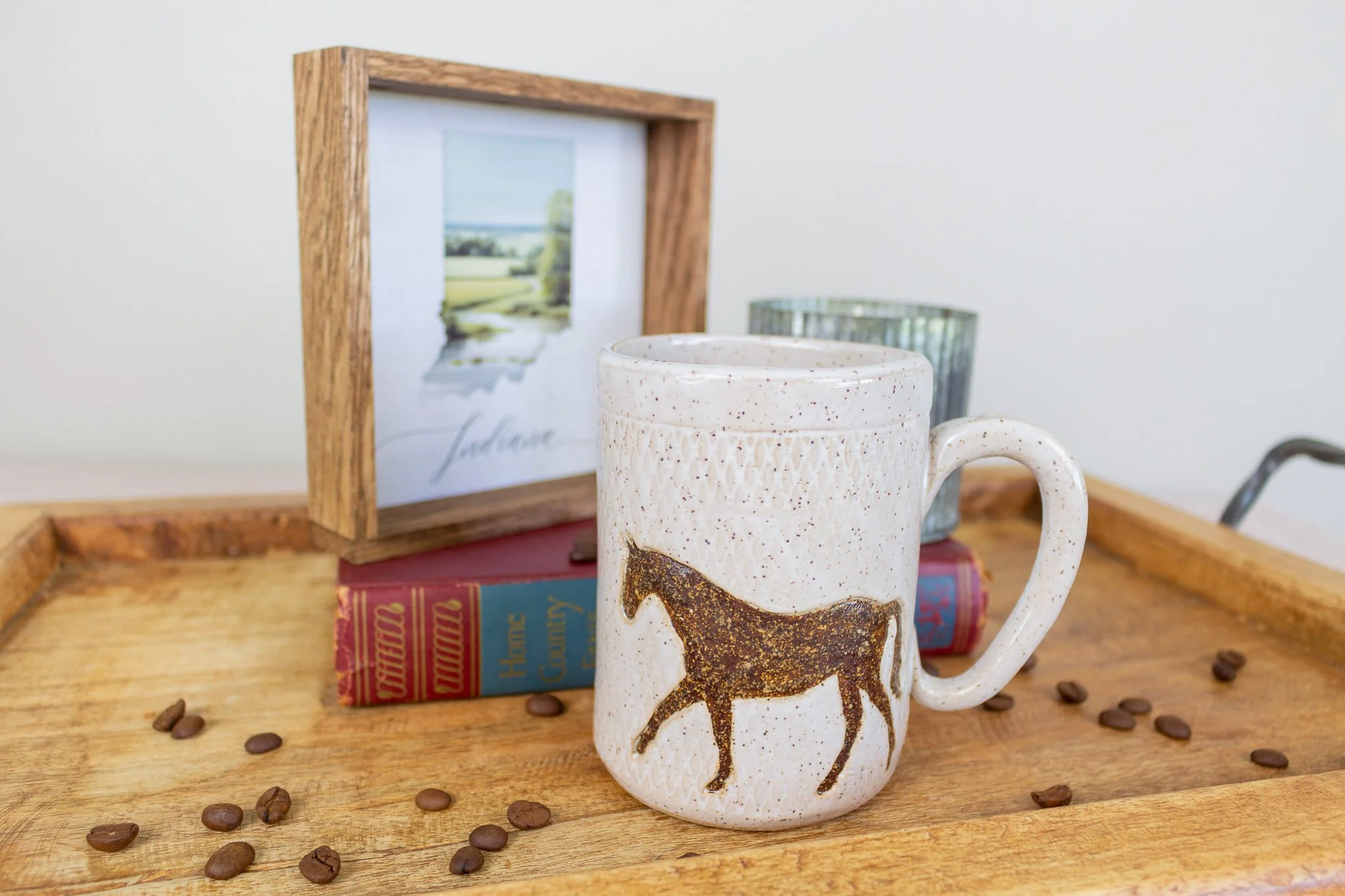 brown and cream horse mug on tray with coffee beans and in front of "Indiana" artwork.