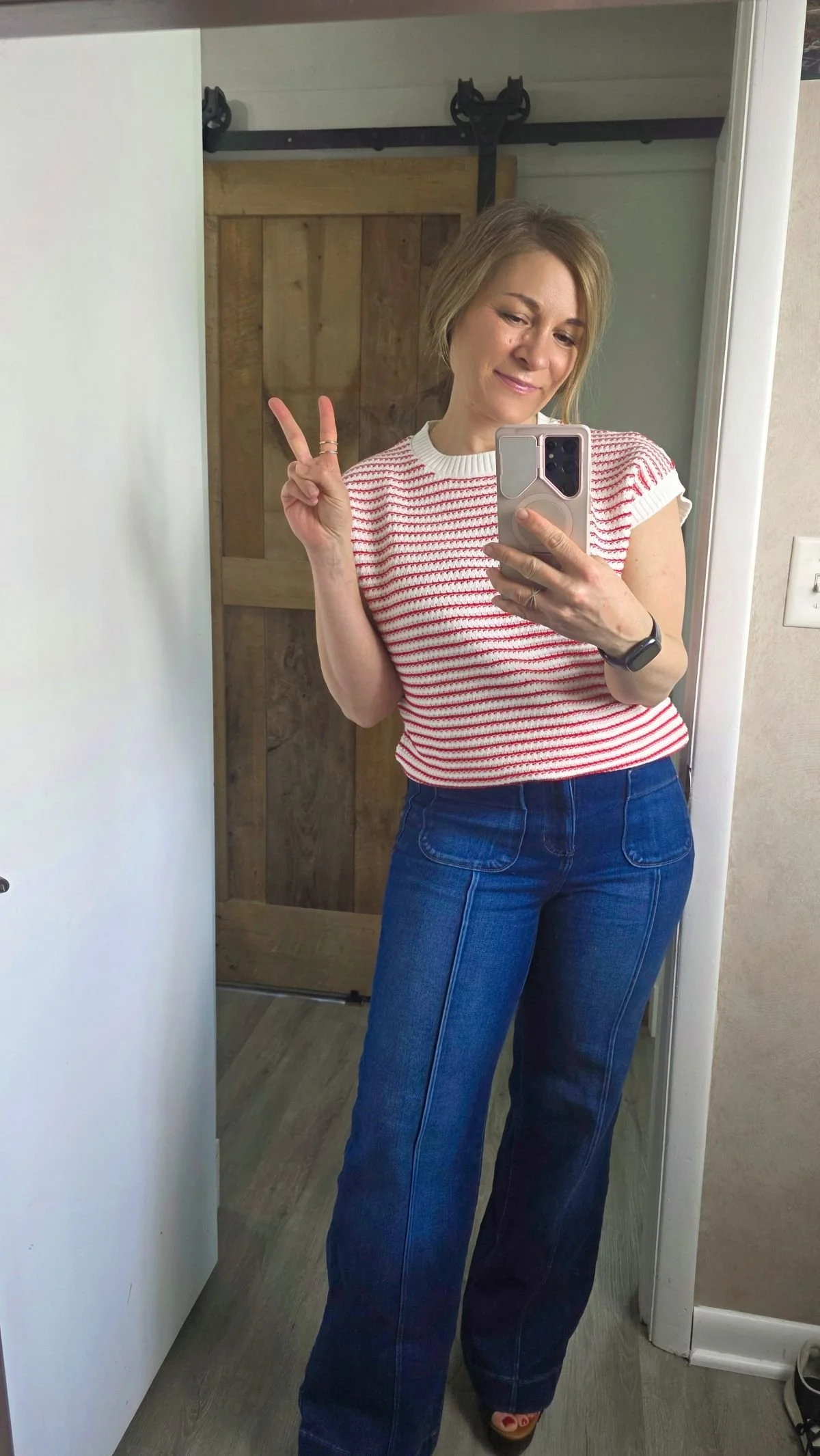 mirror selfie of woman wearing red and white top, giving the peace sign.
