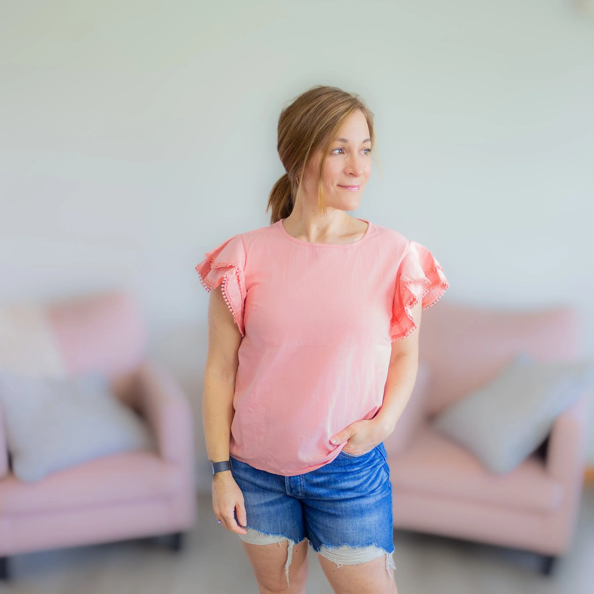 woman looking slightly to side wearing pink top with ruffled sleeves.