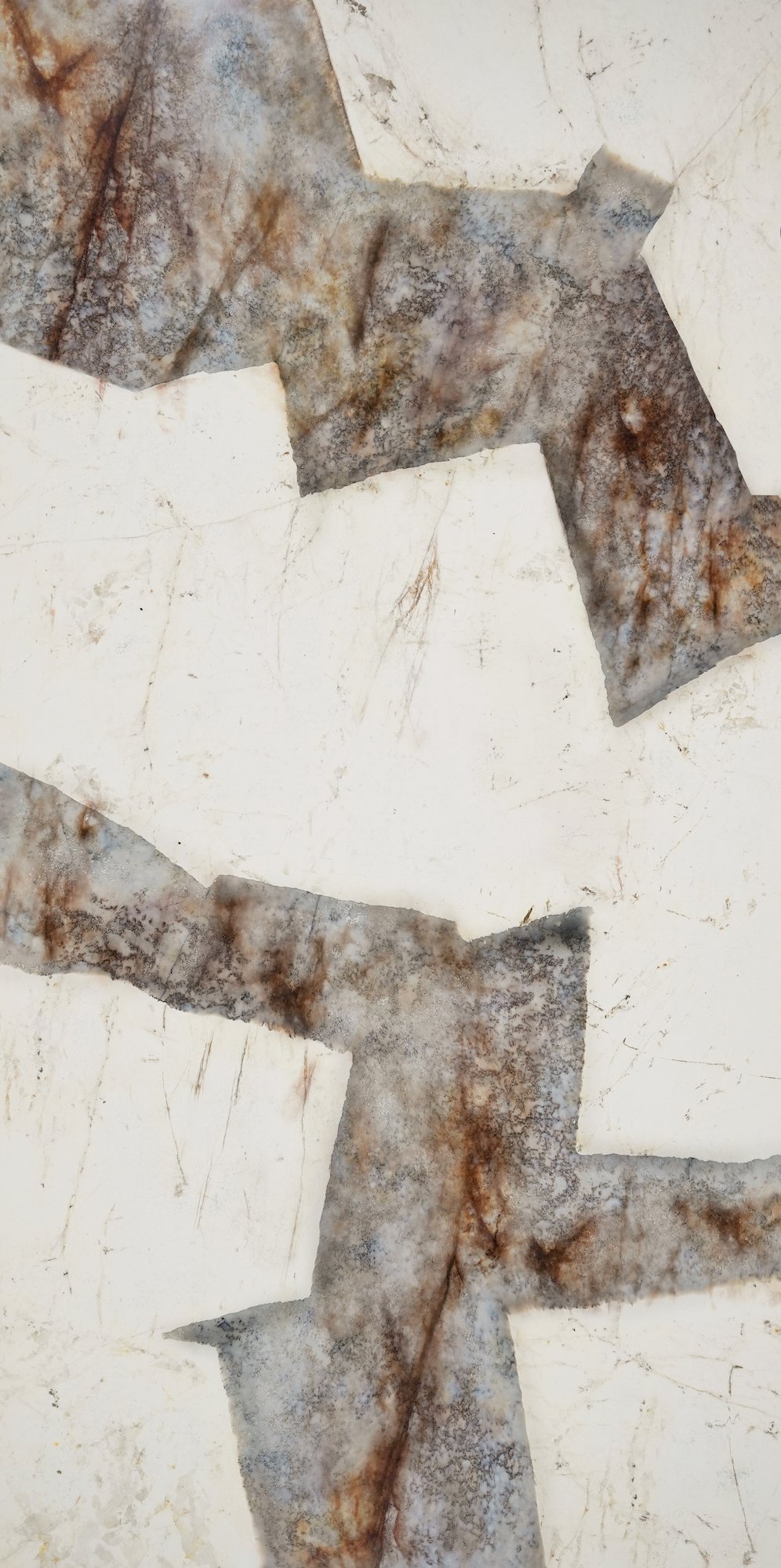 Close-up of a textured stone or marble surface with a pattern of colors including white, gray, and rust, with some areas appearing chipped or weathered.