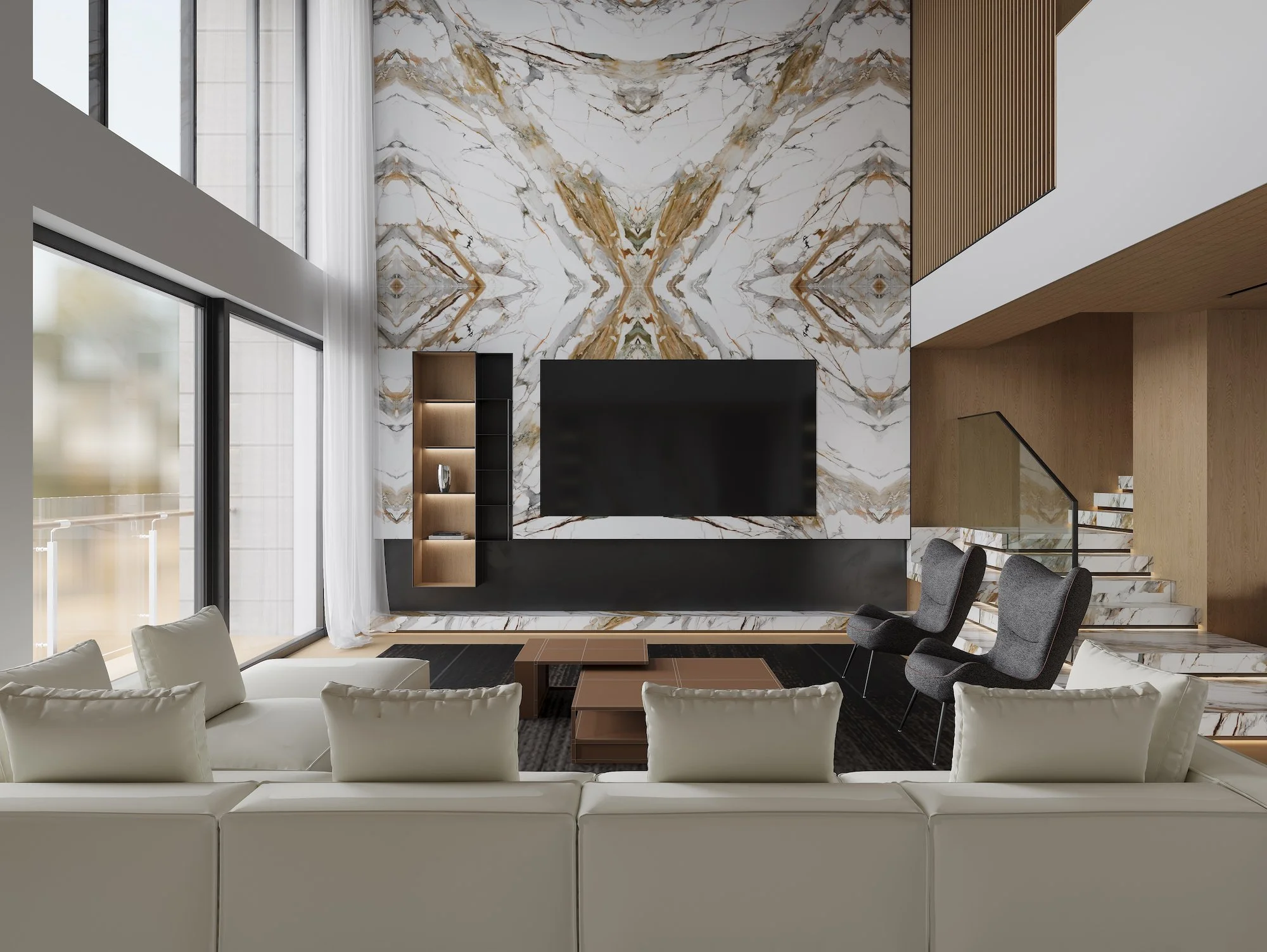Modern living room with a large flat screen TV on a marble accent wall, white sofa, two gray armchairs, a coffee table, floor-to-ceiling windows with white curtains, a staircase, and wooden accents.