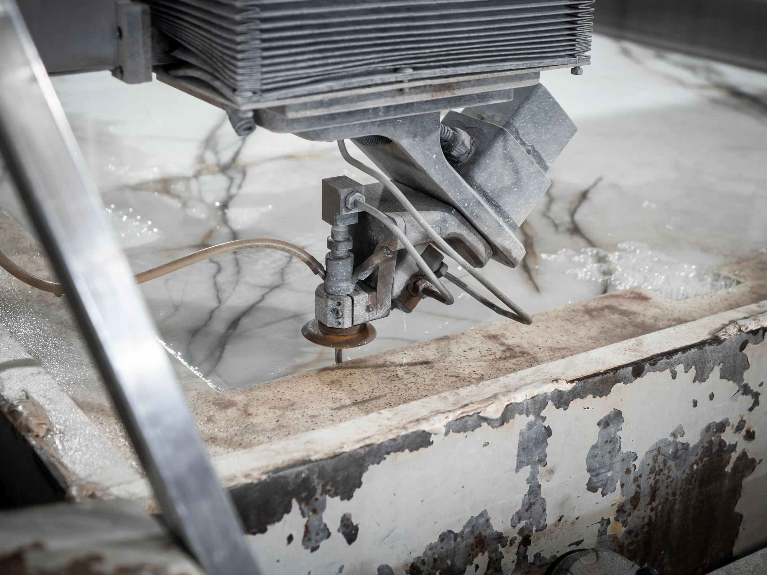 Close-up of a CNC milling machine cutting into marble, showing metal parts and chips on a textured surface.