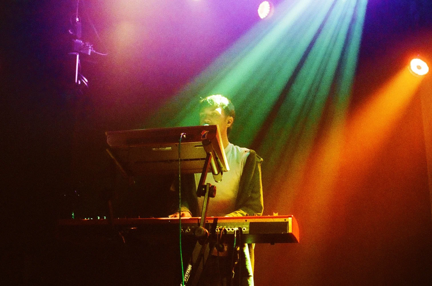 A person playing a keyboard on stage with colorful lights shining down.