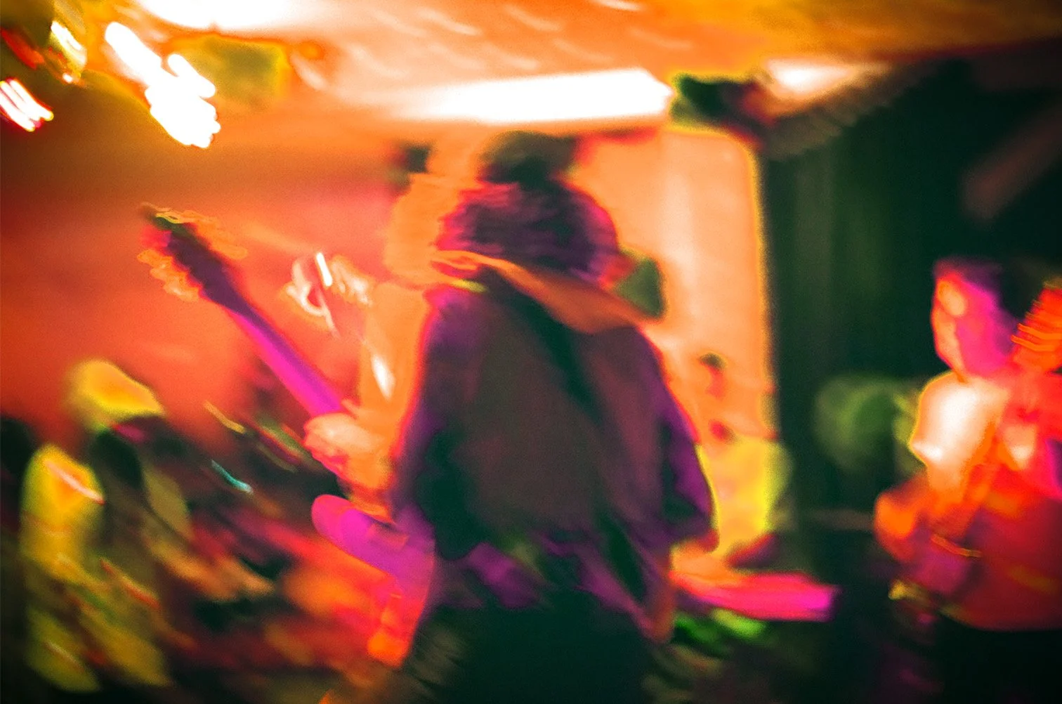 Blurry photo of a person playing guitar in a dimly lit room with colorful lights.
