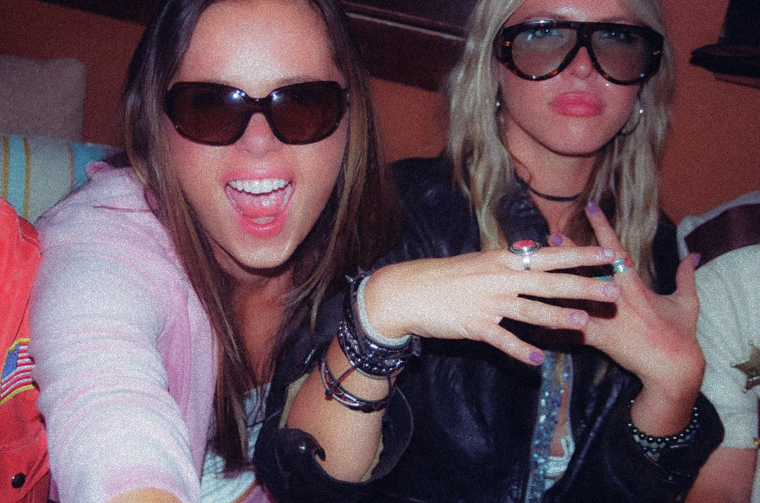 Two women wearing sunglasses, smiling and taking a selfie at a party or social gathering.