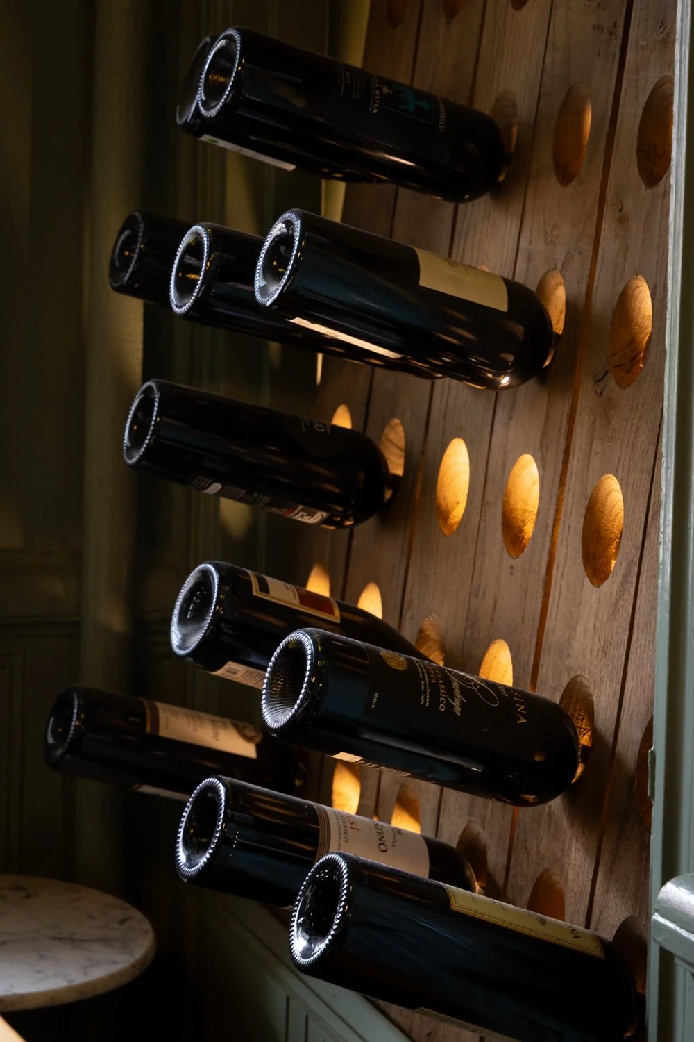 Six bottles of red wine on a wooden table, lit by warm ambient lighting.