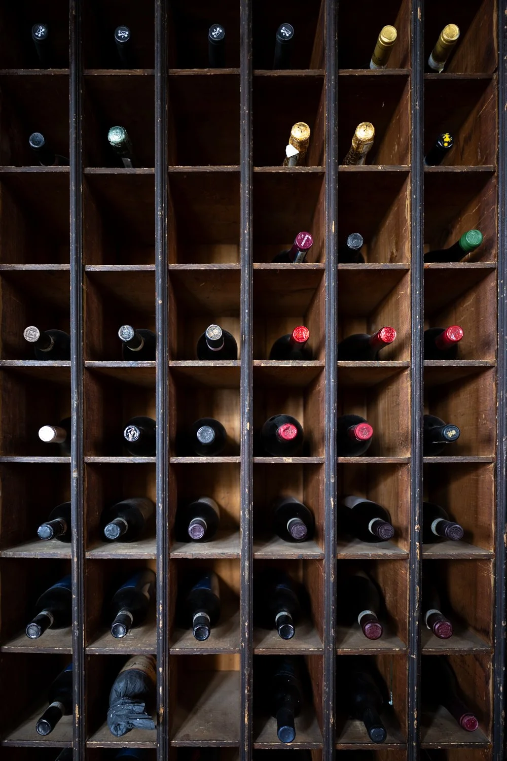 Wooden wine rack holding multiple bottles of wine stored horizontally, with various colored caps.