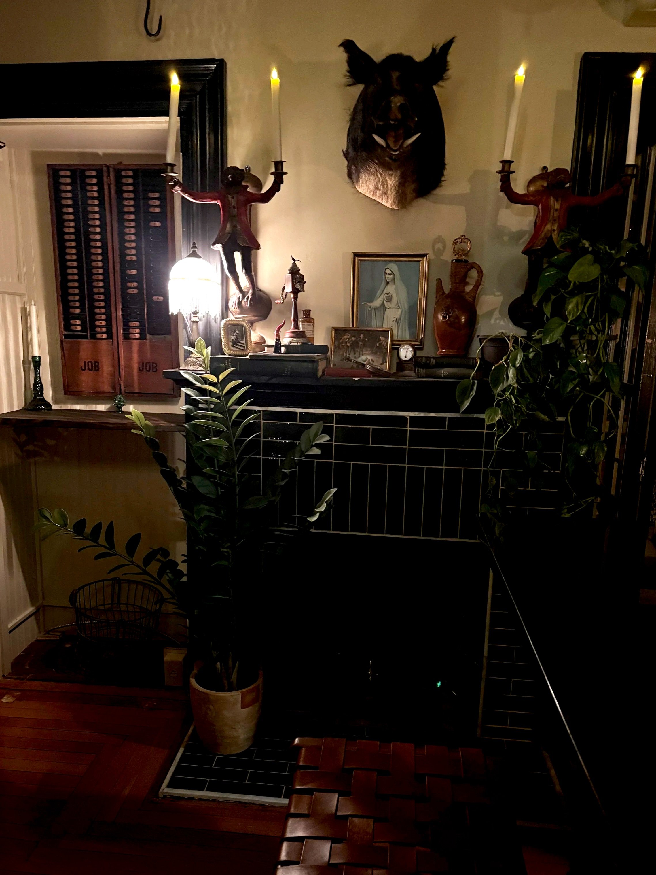 Decorative display with mounted animal head, candles, framed religious image, and various decorative items on a black tiled surface in a dimly lit room.