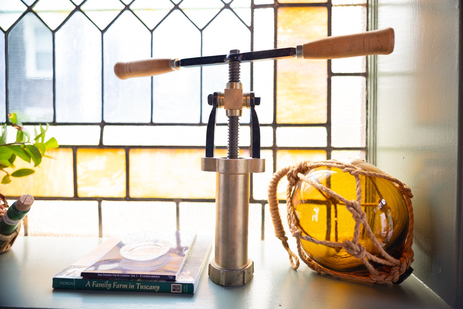 A vintage corkscrew corks the scene with a yellow glass float and books on a windowsill.
