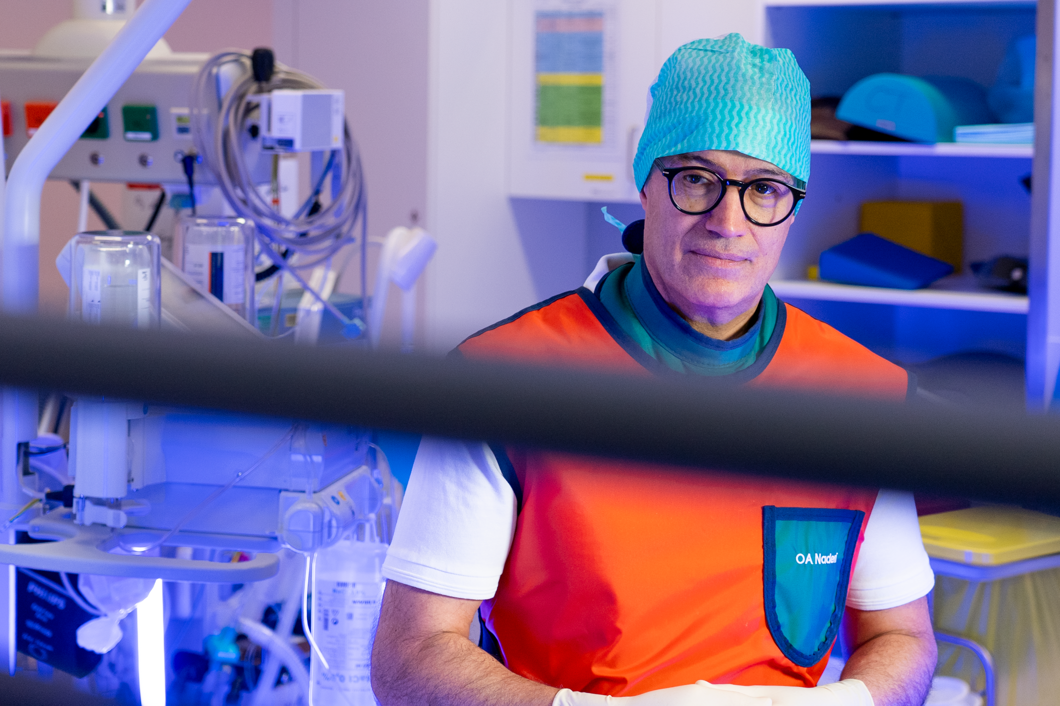 Ein Arzt in OP-Bonnet und Brille in einem Krankenhauszimmer mit medizinischer Ausrüstung.