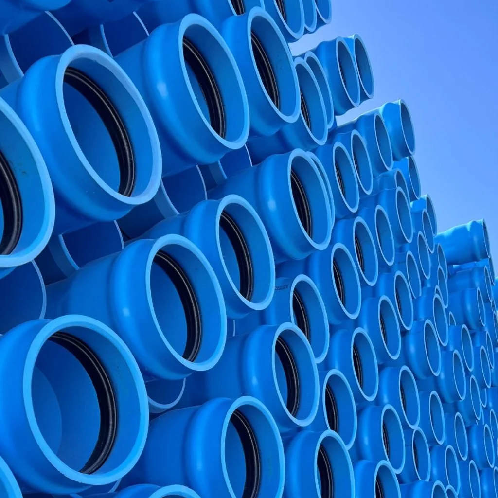 Stacked blue PVC pipes with black seals, arranged in an orderly pattern against a clear sky.