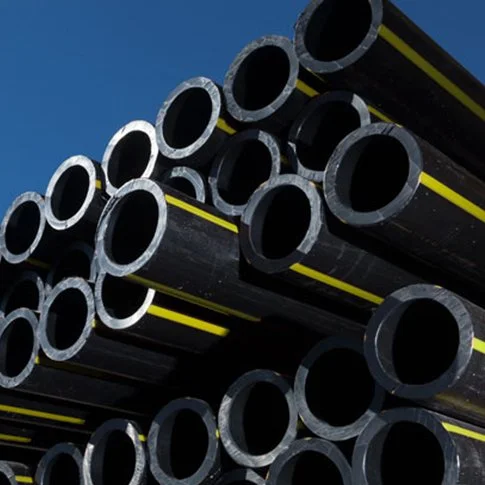 Stacked black industrial pipes with yellow markings against blue sky