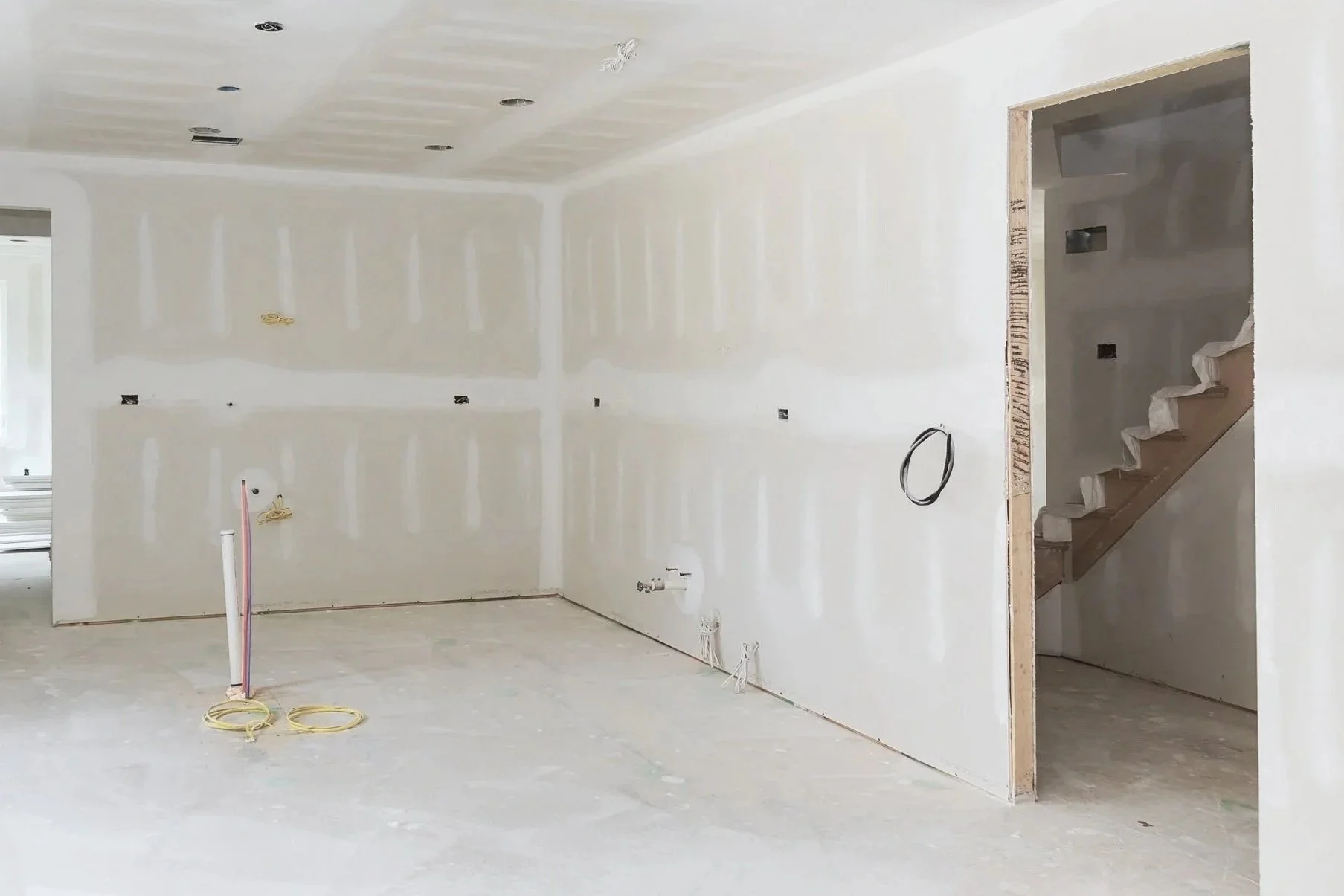 An unfinished room in a house under construction with drywall installed and electrical wiring visible, including a staircase leading to an upper floor in central iowa.