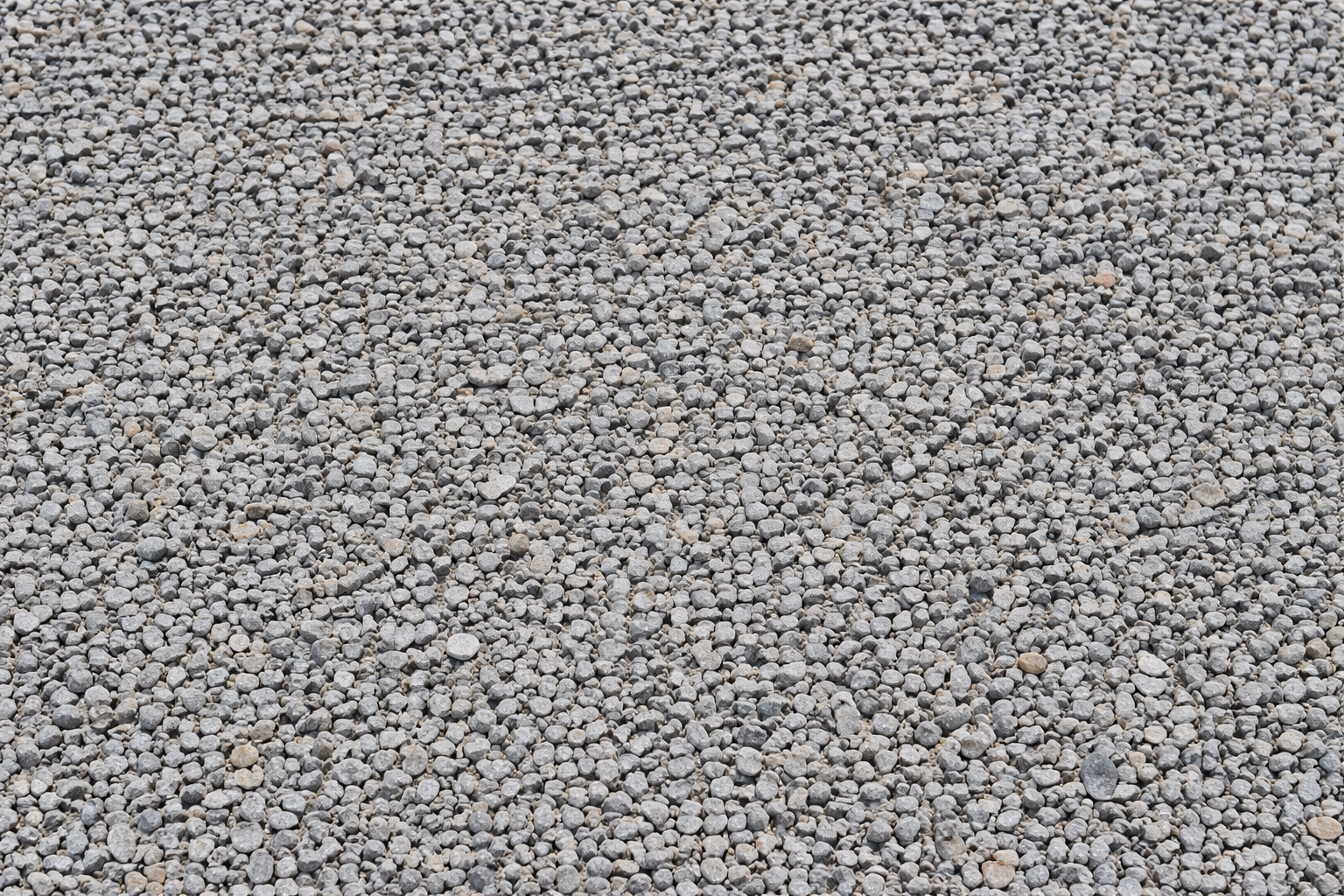 Close-up view of a gravel surface with small, rounded stones in shades of gray, beige, and brown.