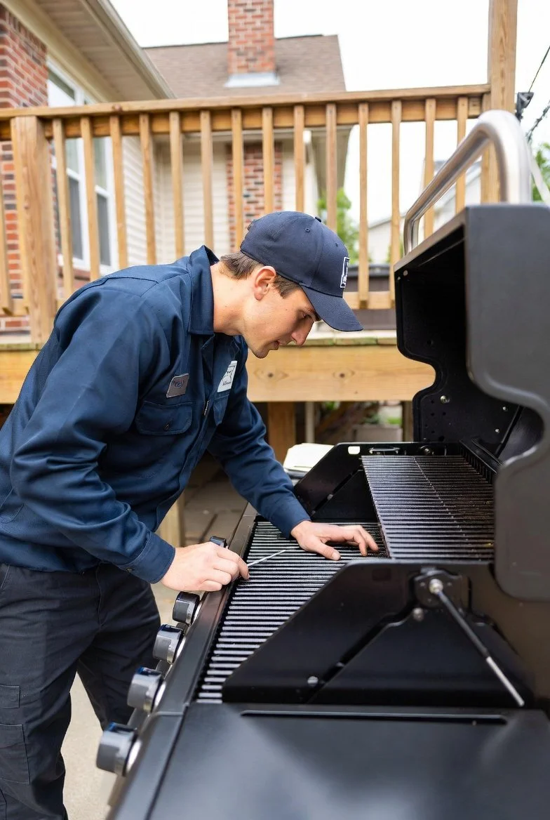 Professional grill cleaning technician in branded overalls following industry standards during BBQ grill inspection and repair