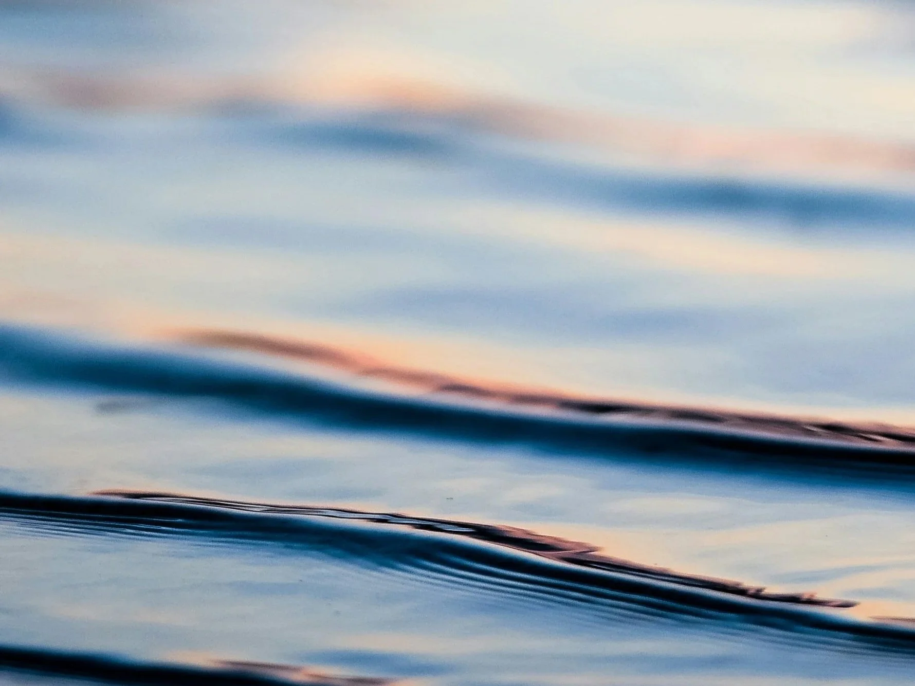 Close-up of calm water with gentle ripples and soft pastel reflections from the sky.