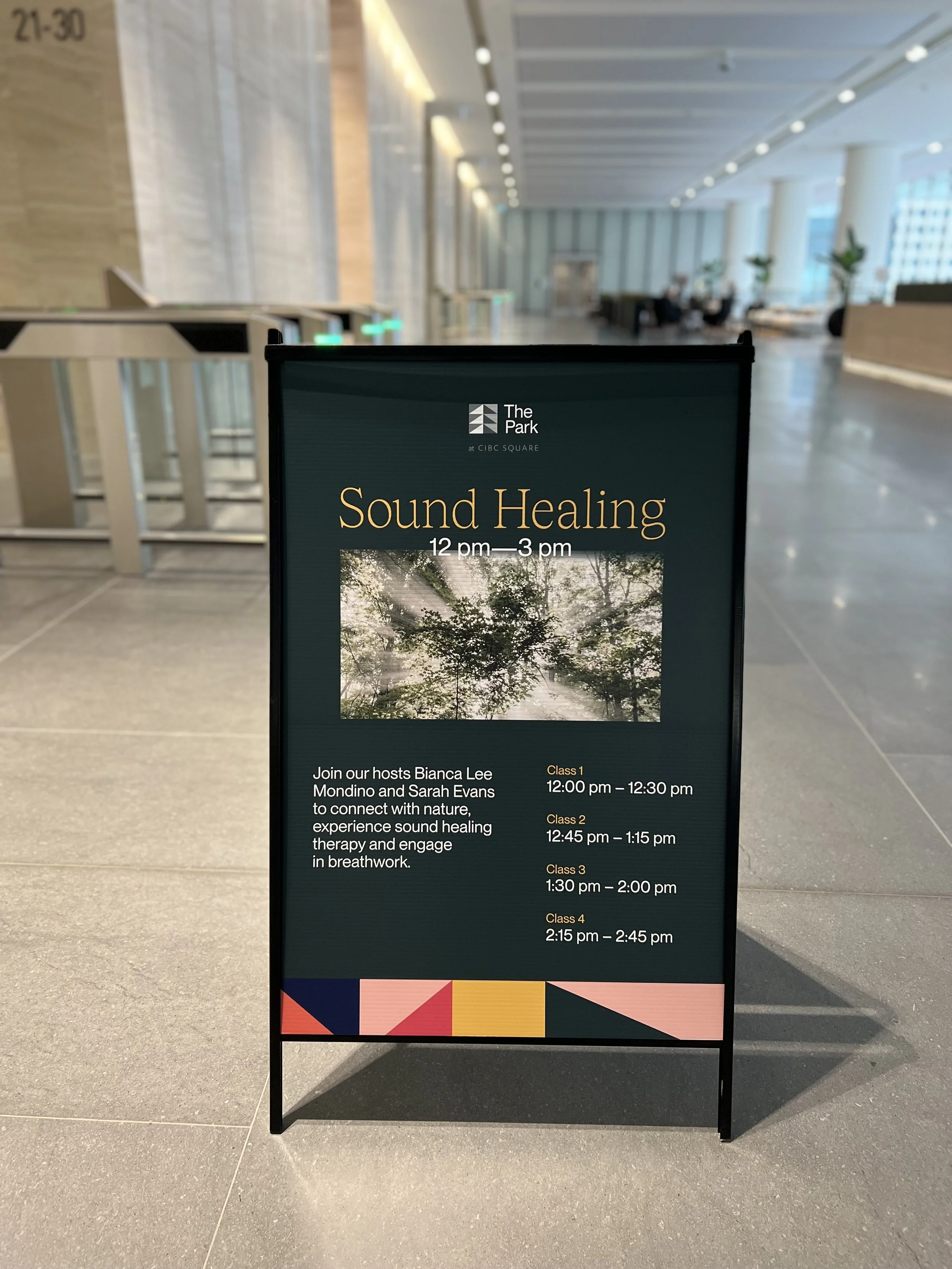 A sign advertising a sound healing event at The Park, CIBC Square. The event lasts from 12 pm to 3 pm with four classes scheduled at 12, 12:45, 1:30, and 2:15 pm, hosted by Bianca Lee Mondino and Sarah Evans. The sign features an image of sunlight filtering through tree branches.