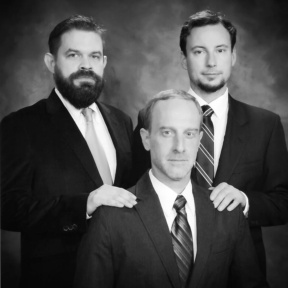 Black-and-white studio portrait of John Sutton, Ben Beres, and Zac Culler in suits, posed in a vintage family-portrait style referencing their ongoing project titled Sears Portraits.