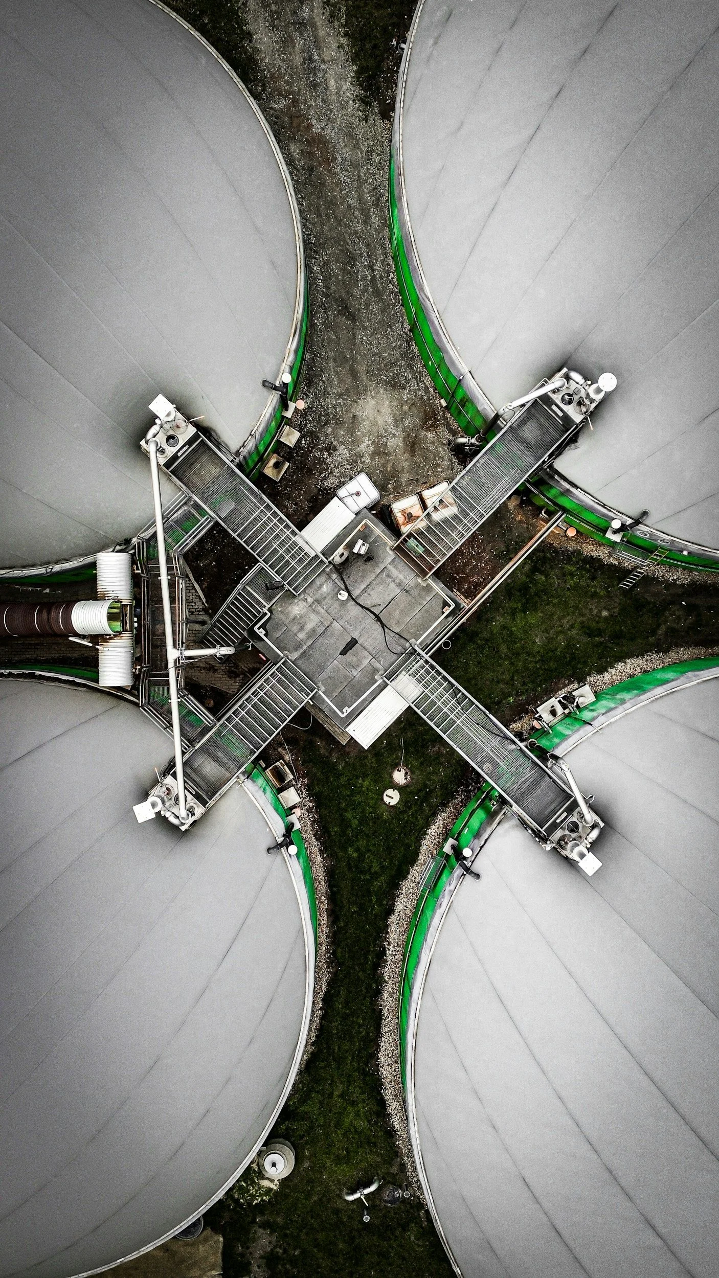 Luftaufnahme von vier großen Silos, verbunden durch metallische Treppen und Plattformen, mit einem geordneten Weg in der Mitte.