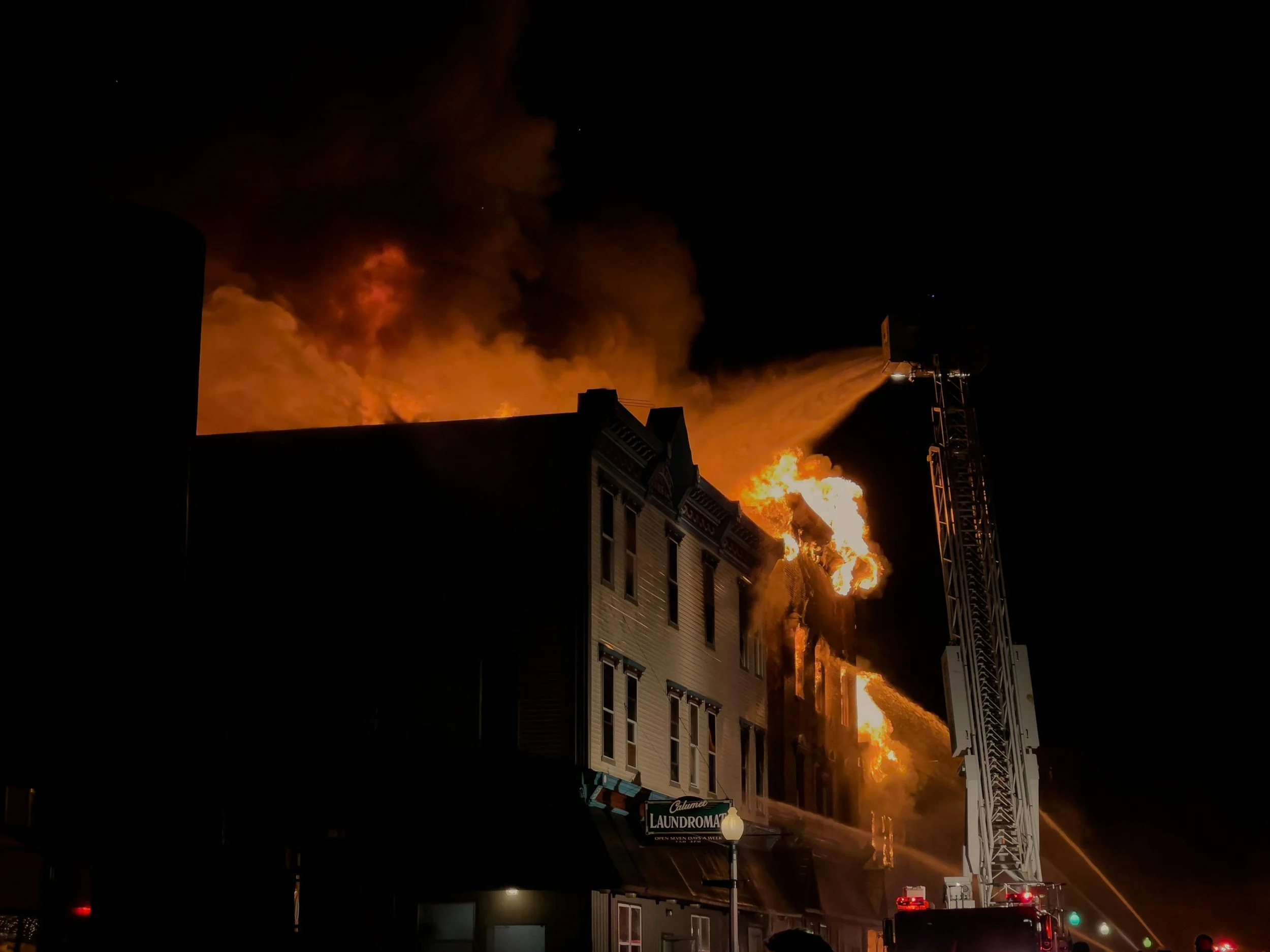 Ein Brand in einem mehrstöckigen Gebäude in der Nacht, Feuerwehr löscht die Flammen mit einem Wasserstrahl aus einem Leiterwagen.