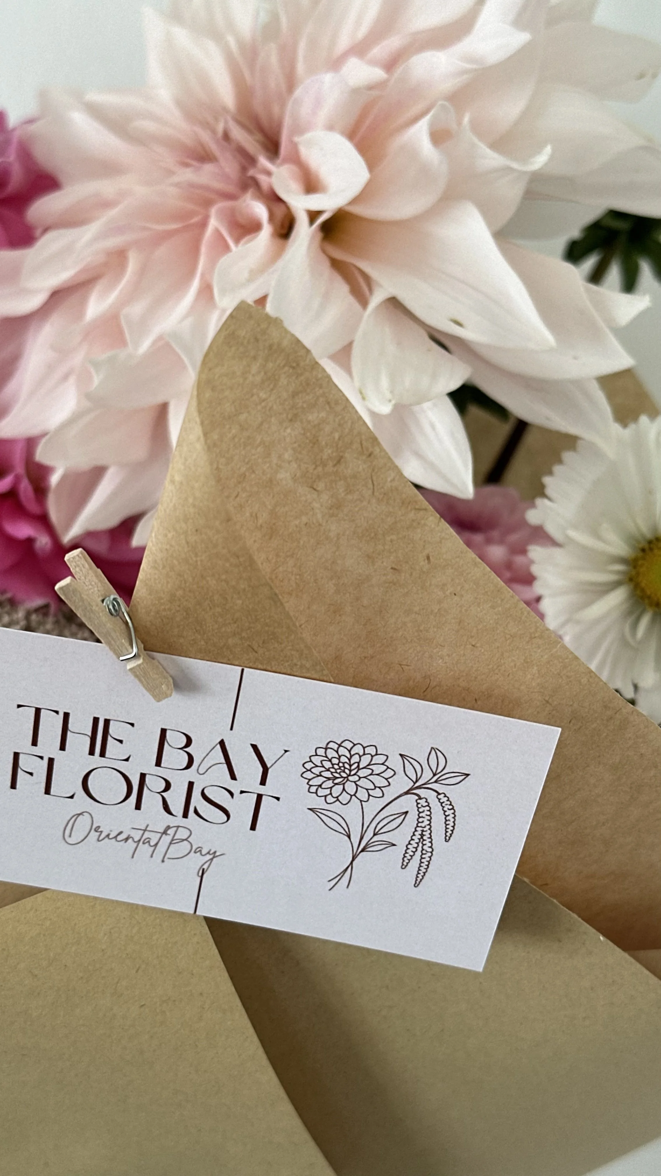 Close-up of a bouquet of pink and white flowers with a business card from The Bay Florist attached with a small clothespin.