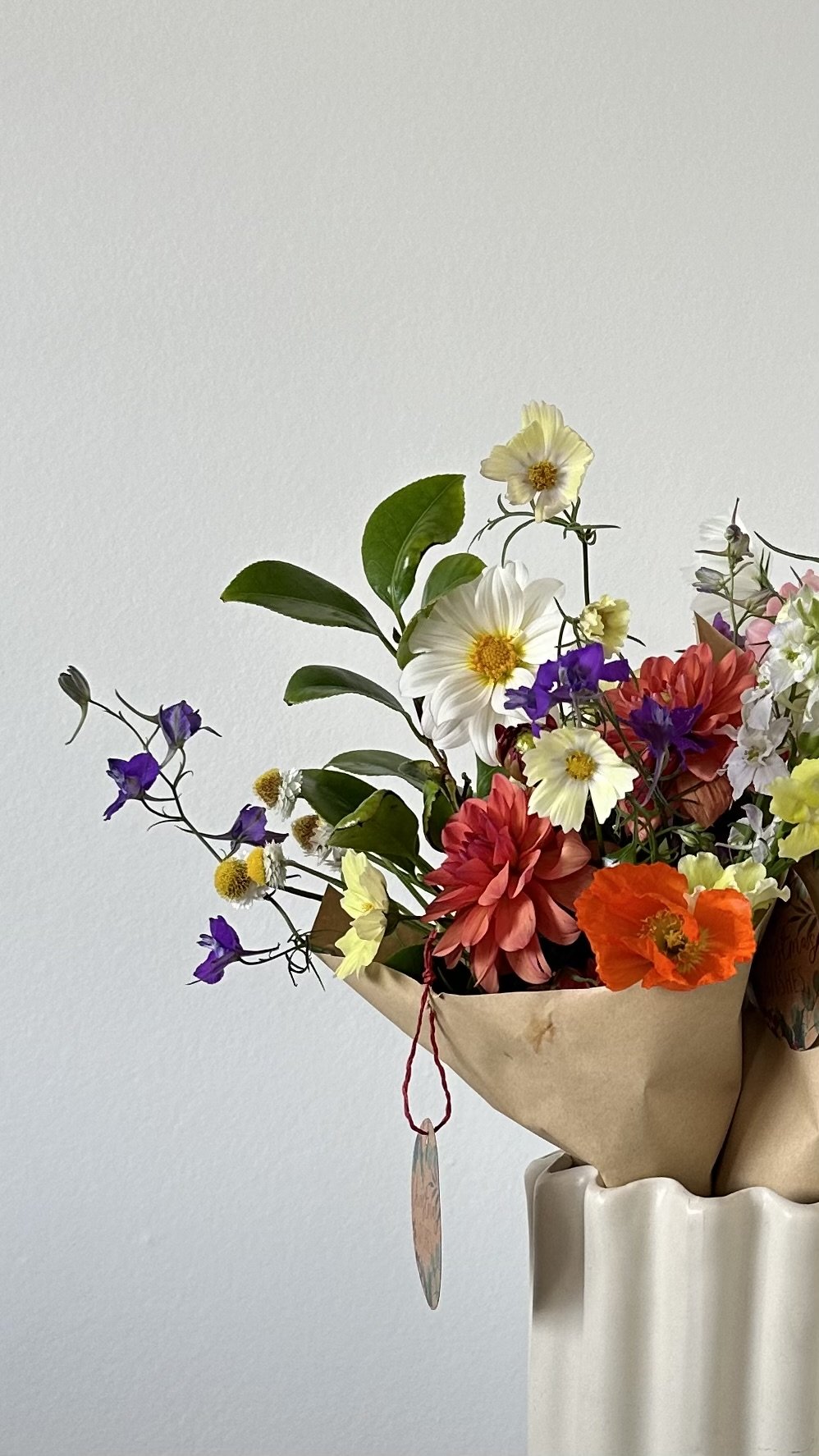 Colorful bouquet of various flowers in a paper wrap in a white vase.