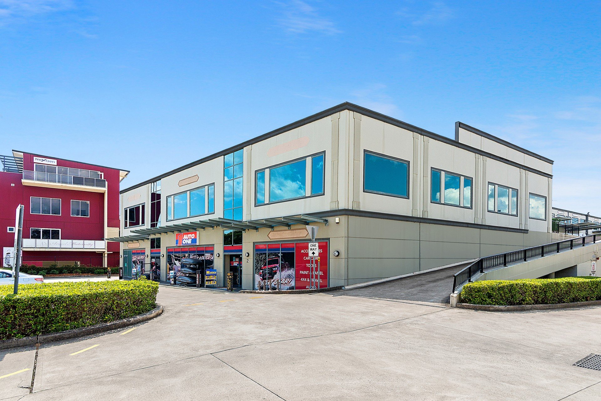 Exterior view of an Auto One store in a multi-story shopping center under a blue sky.